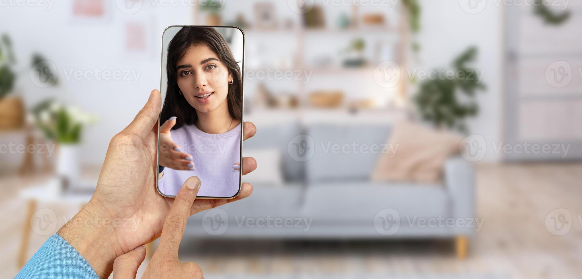 A person connects with someone through a smartphone during a call. The setting is a cozy home with a light-filled living room. The interaction appears warm and engaging. photo