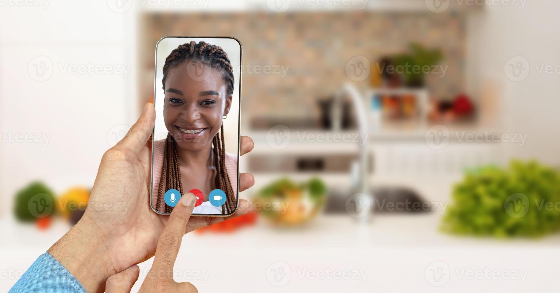 A person is enjoying a call on a smartphone from their kitchen. The screen shows a smiling individual, highlighting the connection made through online communication. photo