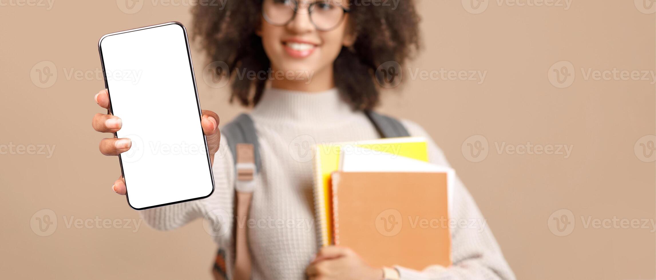 Education, knowledge and technology. Smiling millennial african american woman in glasses with backpack, smart watch and notebook makes selfie on phone after covid-19 pandemic, blurry, studio shot photo