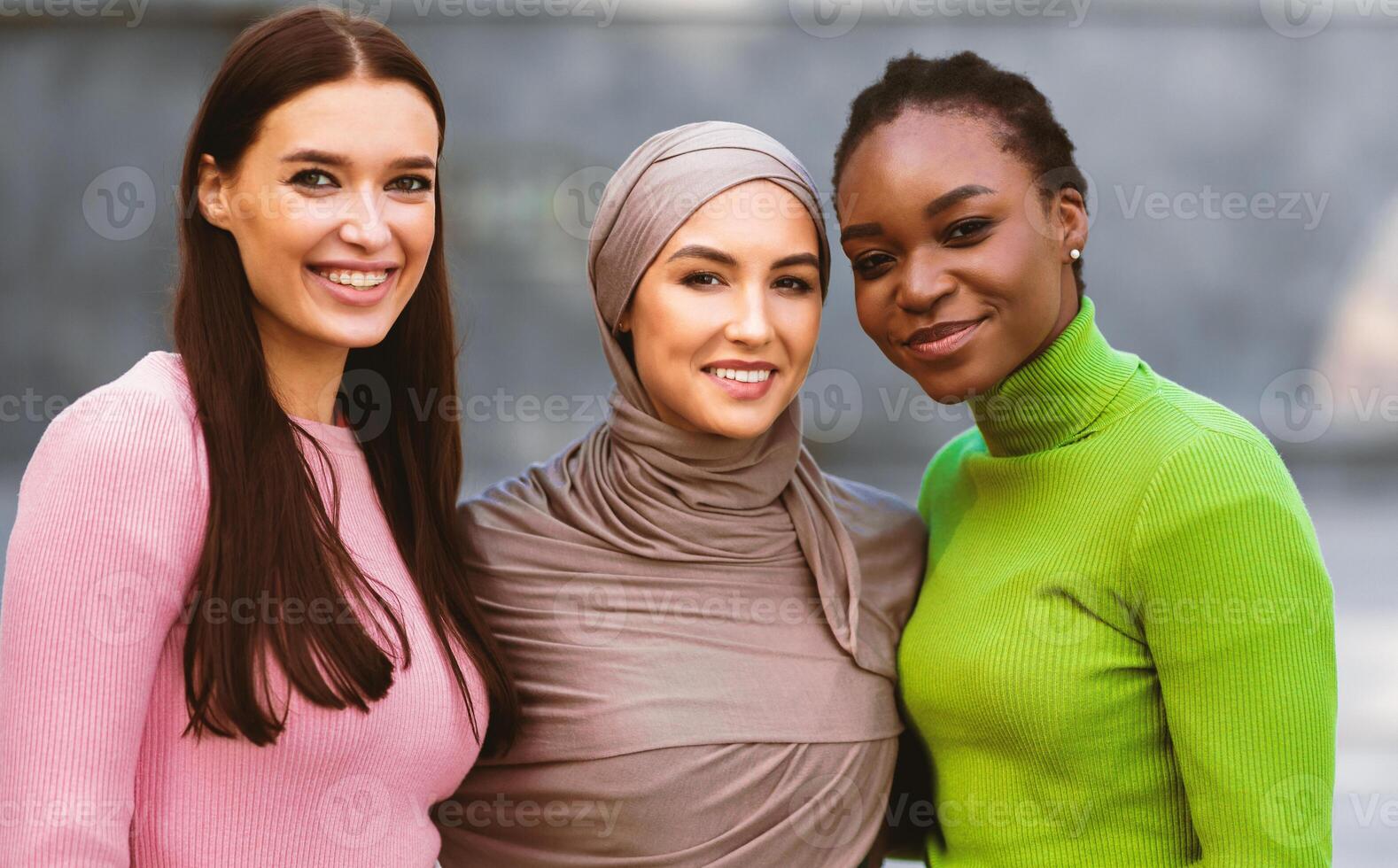 Portrait Of Three Multiracial Young Women. African American, Muslim And Caucasian Ladies Posing Hugging Together Standing Outside, Smiling Looking At Camera. Females Unity And Diversity photo