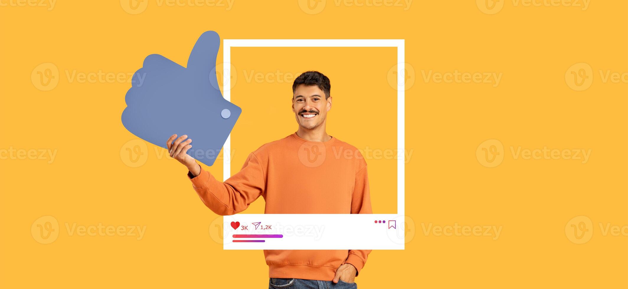 A man in an orange sweater expresses positivity by giving a thumbs up while holding a large like symbol. Bright yellow background enhances the cheerful vibe, perfect for social media engagement. photo