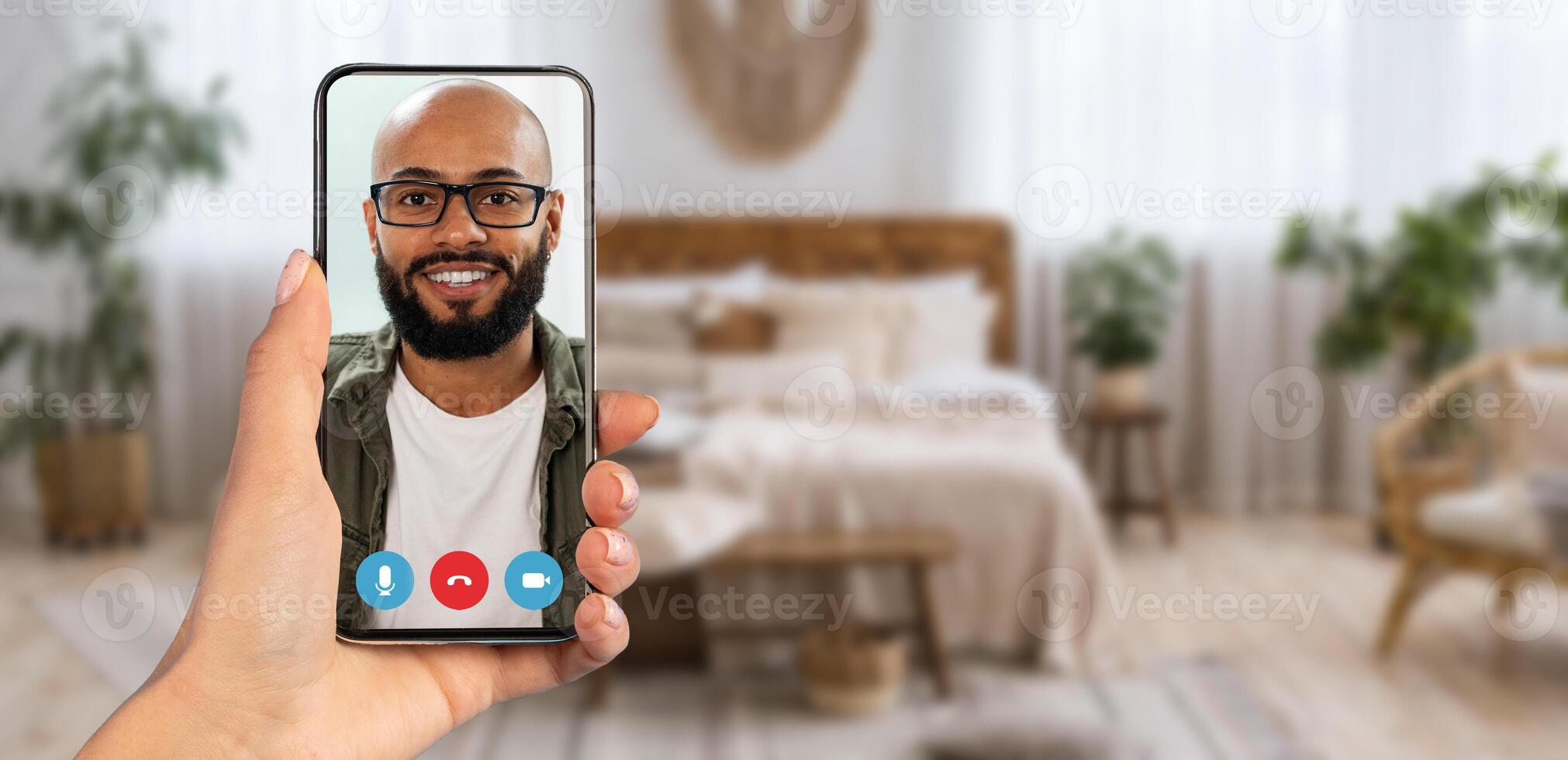 A person enjoys a call with a smiling individual on their smartphone, showcasing a comfortable home environment filled with plants and cozy decor. photo