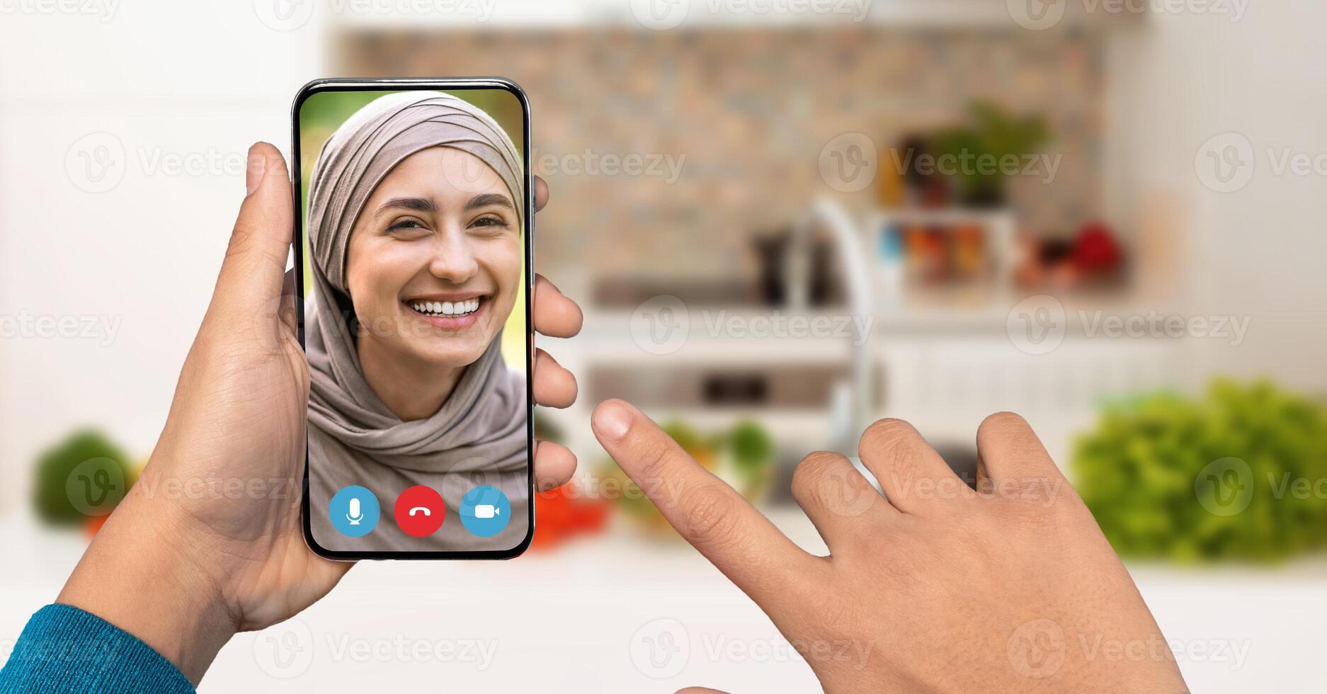 A person smiles while engaging in a call on their smartphone, showcasing a friendly interaction. The cozy kitchen background adds warmth to the conversation. photo