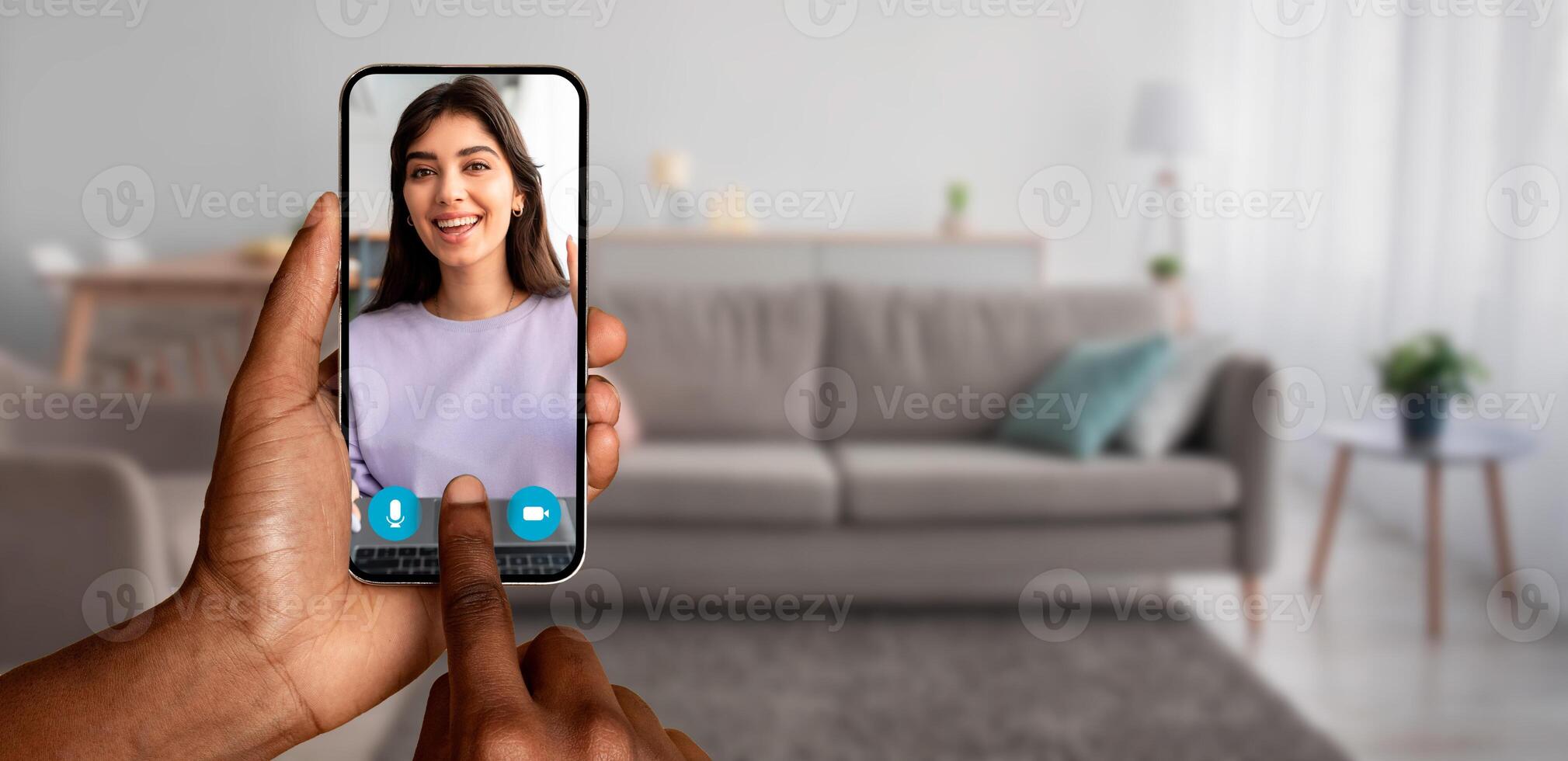 A person holds a smartphone displaying a smiling friend during an online call in a cozy living room. The scene captures modern communication and connection from home. photo