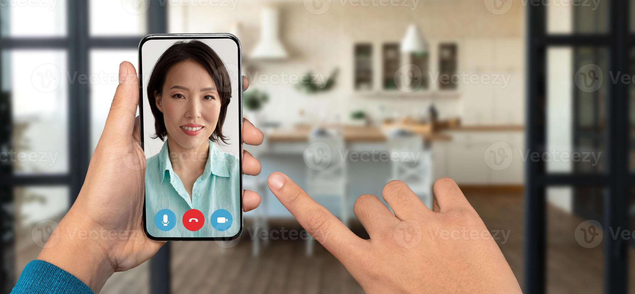 Close-up of a hand holding a smartphone during a call. A woman appears on screen, smiling, while a cozy kitchen setting is visible in the background. The atmosphere feels warm and welcoming. photo