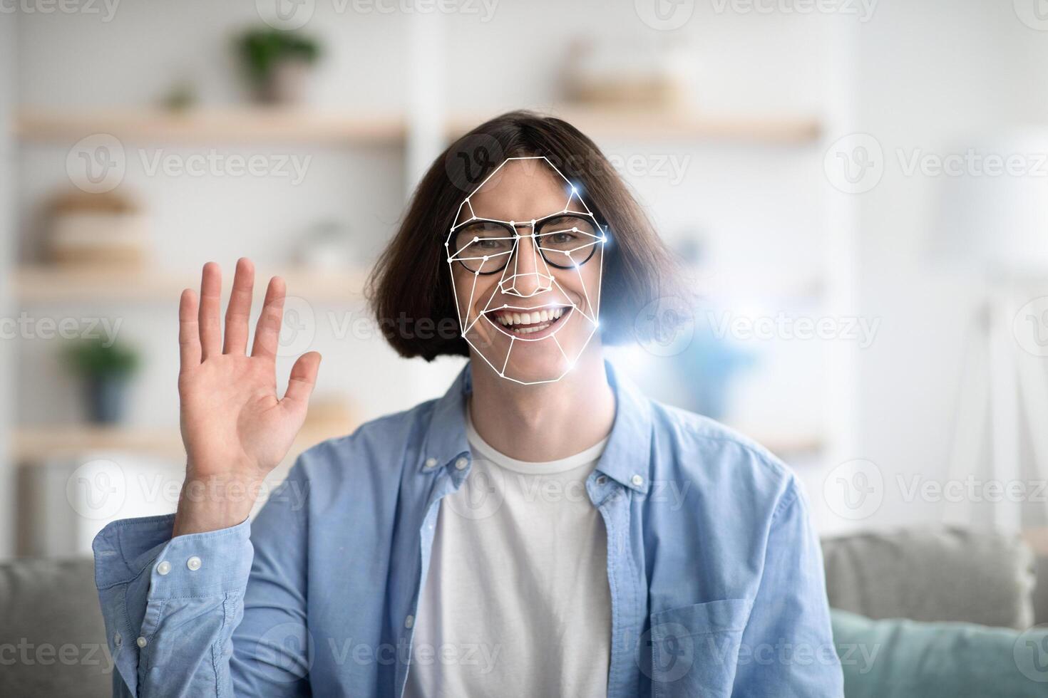 A person with a joyful expression waves while experiencing facial recognition technology at home. This showcases the integration of modern tech in everyday life, emphasizing personal interaction. photo