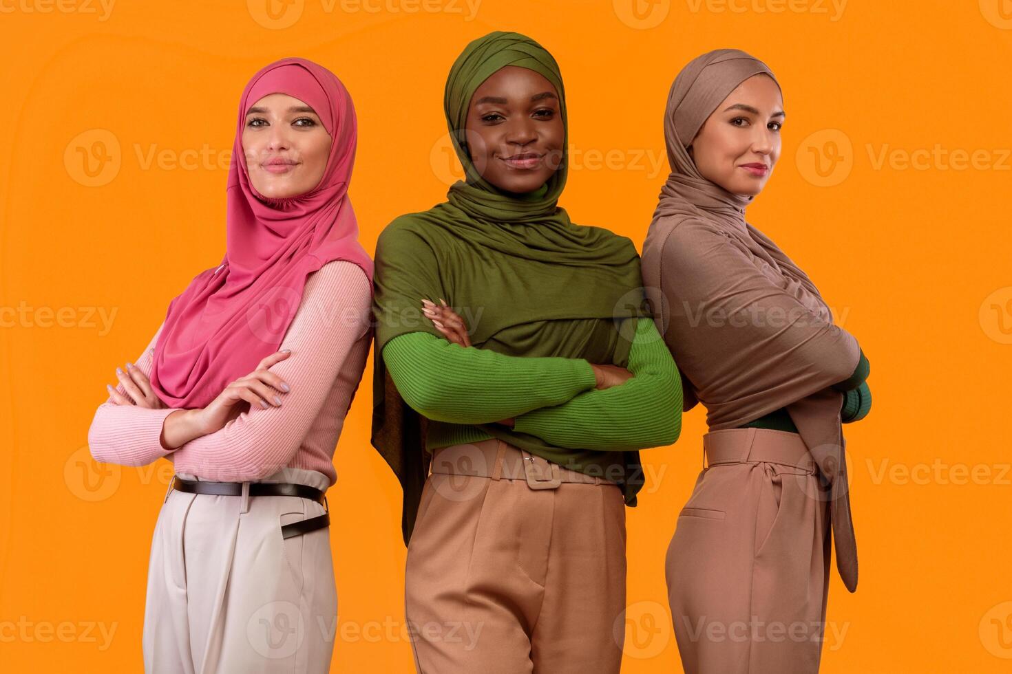 Three Successful Modern Muslim Women In Hijab Crossing Hands Smiling To Camera Standing Over Yellow Studio Background. Arabic Ladies Posing In Headscarf. Islamic Females Diversity Concept photo