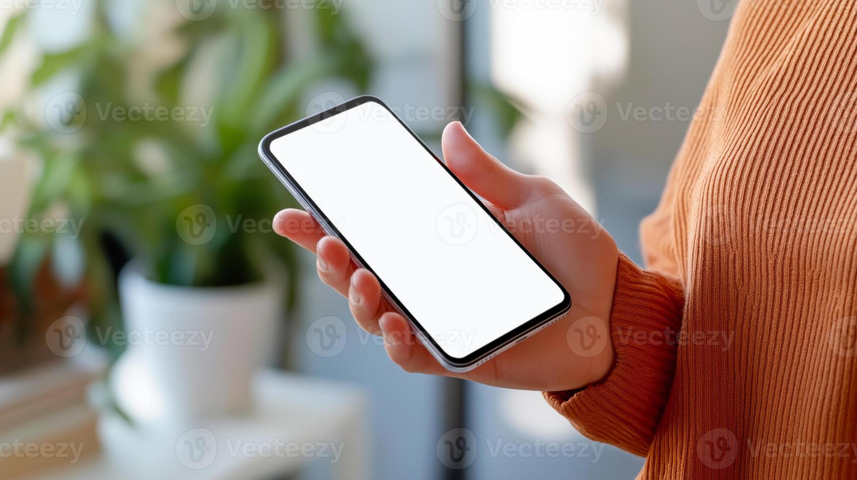 A person holds a smartphone with an empty screen, surrounded by indoor plants. photo