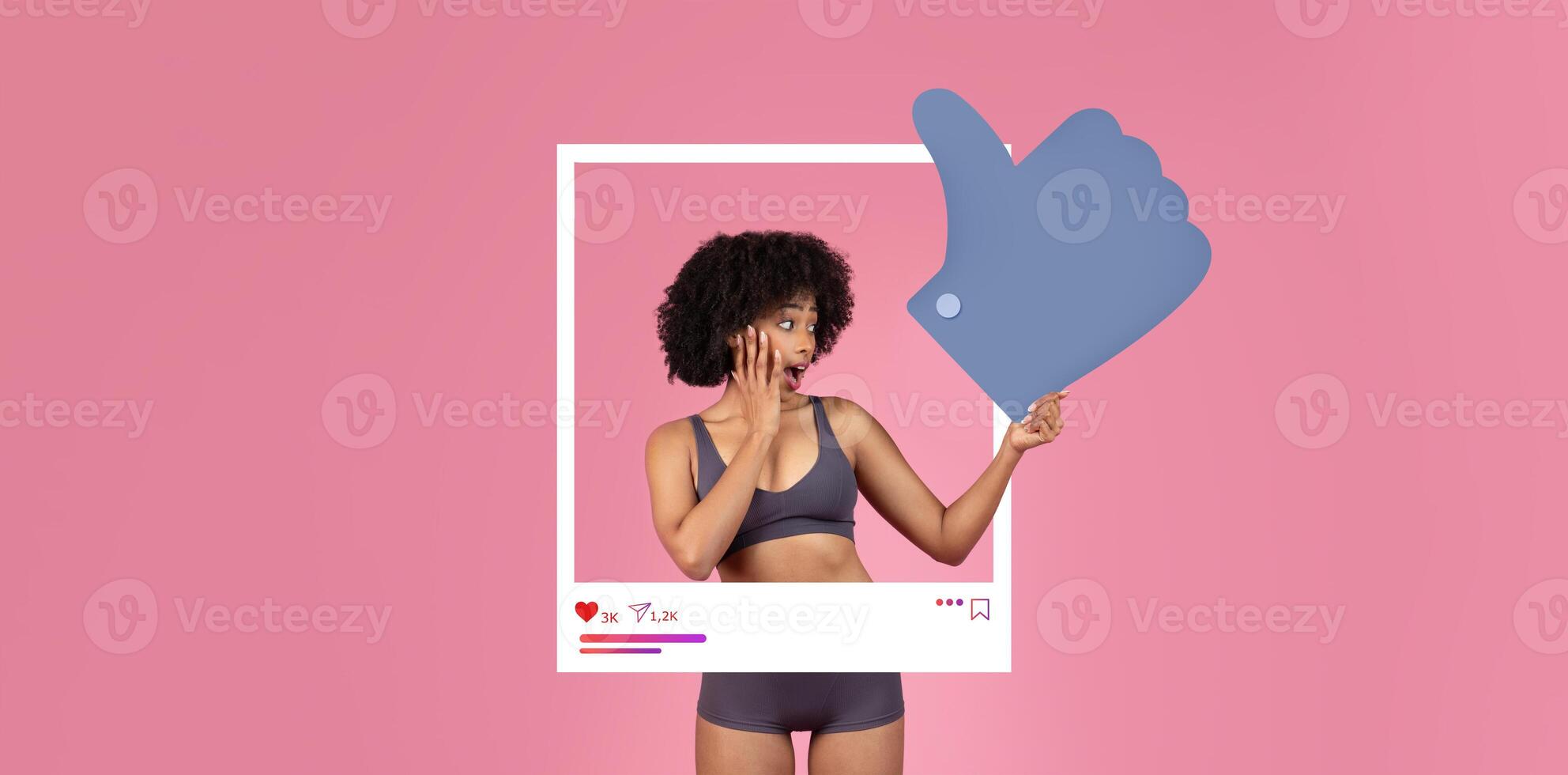 A young woman in a cropped top and shorts expresses surprise while pointing at a large thumbs-up symbol. The vibrant pink backdrop enhances her excitement, showcasing social media interaction. photo