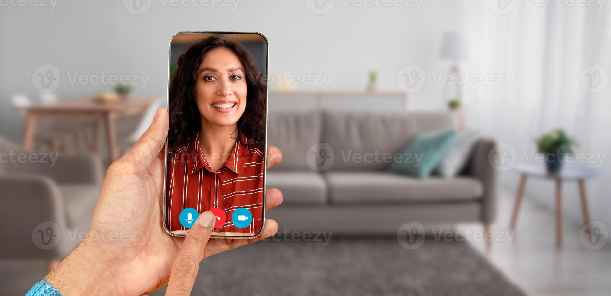 A person participates in a call using a smartphone. The setting is a cozy home with a comfortable sofa in the background and natural light coming in. photo