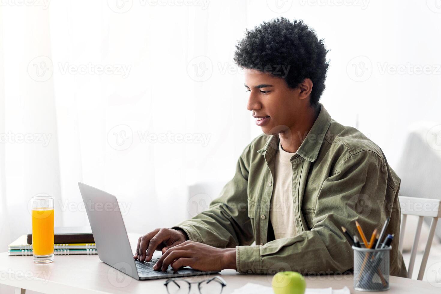 Cheerful black teen guy having conference on laptop with teacher from home. University student attending lecture or online seminar, consulting his teacher, watching lesson photo