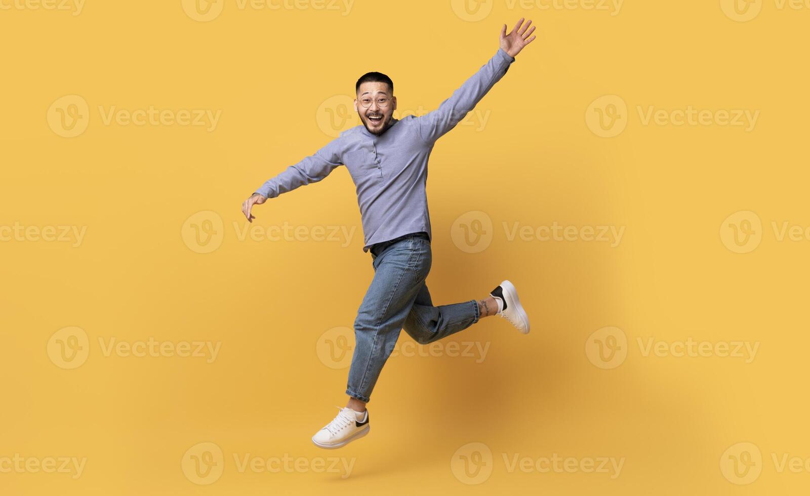 Happy Excited Asian Man Jumping In Air On Yellow Background, In Motion Shot Of Emotional Cheerful Millennial Guy In Casual Clothes Having Fun In Studio, Full-Length Shot With Copy Space photo