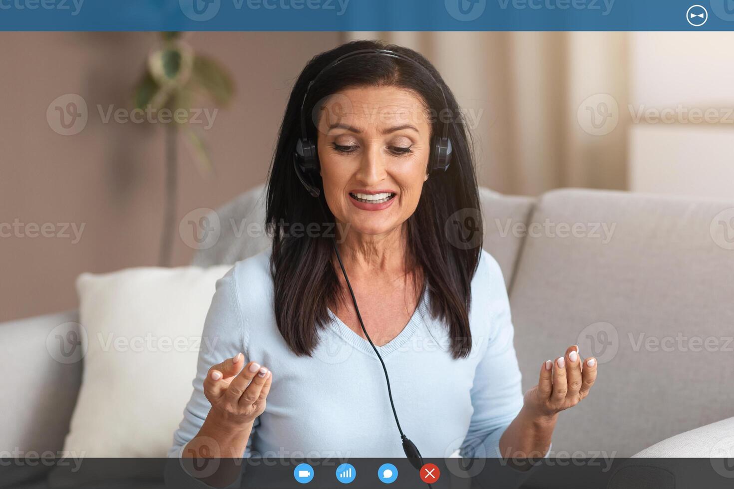 Online Call And Distance Communication. Portrait of senior lady in headphones sitting on sofa at desk, using computer, having virtual conference on laptop talking to webcam, explaining plan photo