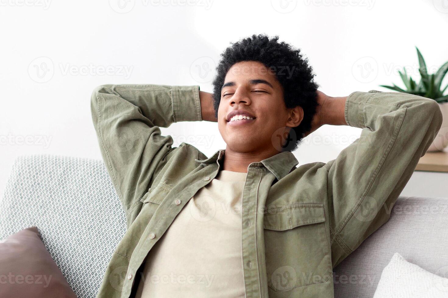 Calm young teen guy relaxing on sofa, napping with closed eyes, feeling peaceful at home, panorama. Positive African American teenager having day off, taking break from work or studies photo