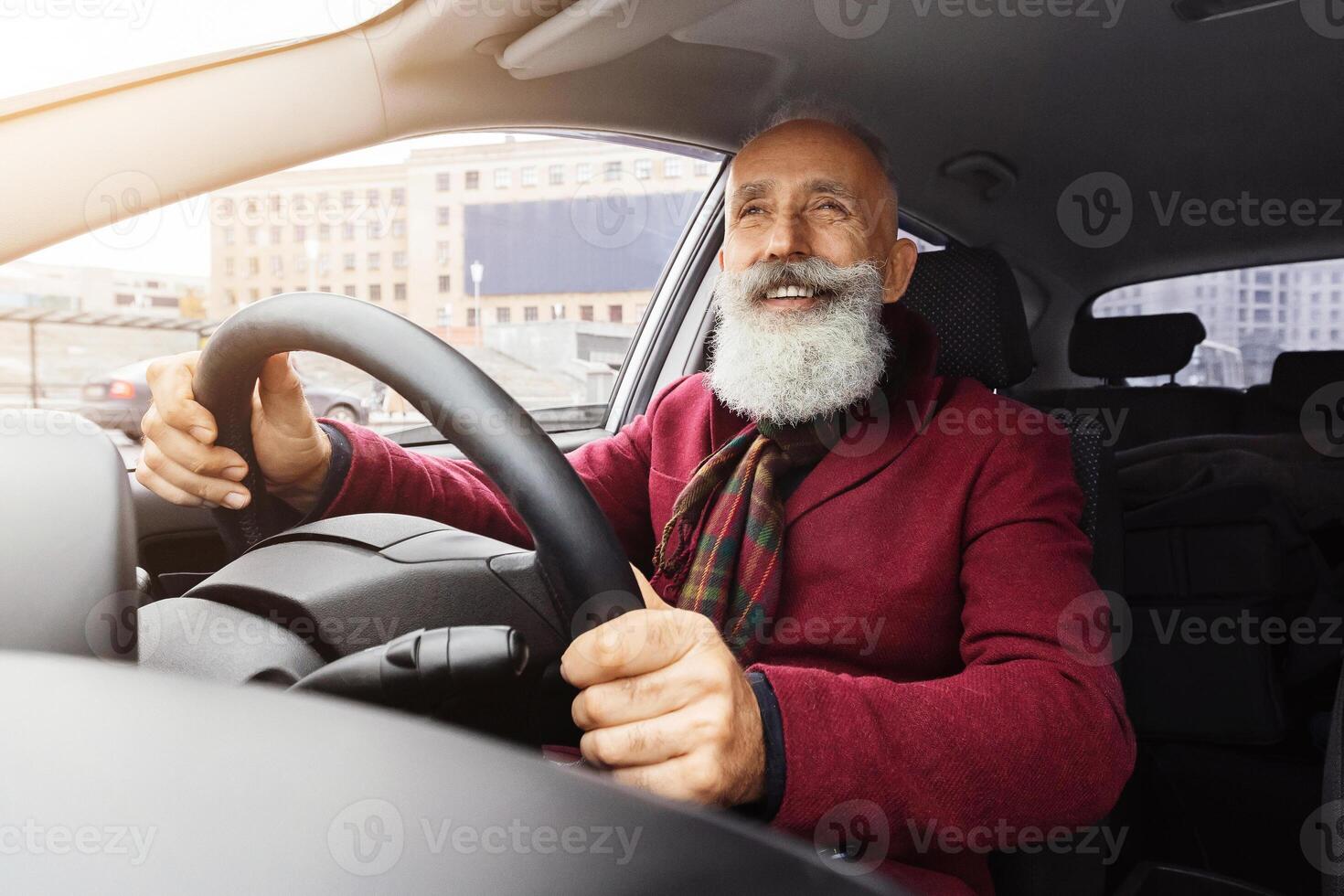 Handsome elderly grey-haired man with long beard sitting inside new car, traveling alone or going to office, senior businessman going to business meeting by his auto, shot from front panel photo
