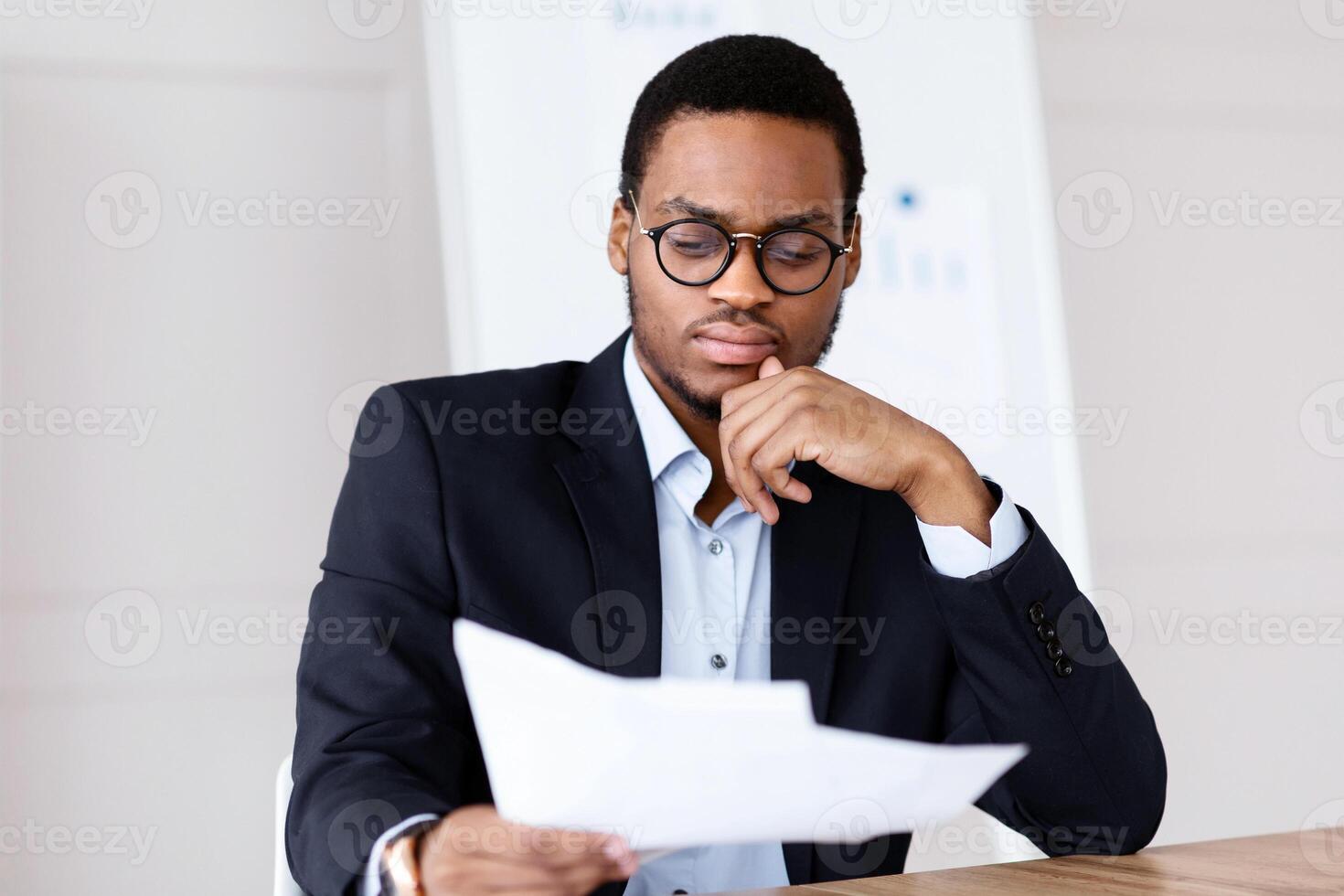 Pensive black manager, businessman sitting in his office in front of laptop, reading papers marketing report, having financial troubles, copy space. Problems with business, bankruptcy, crisis, concept photo