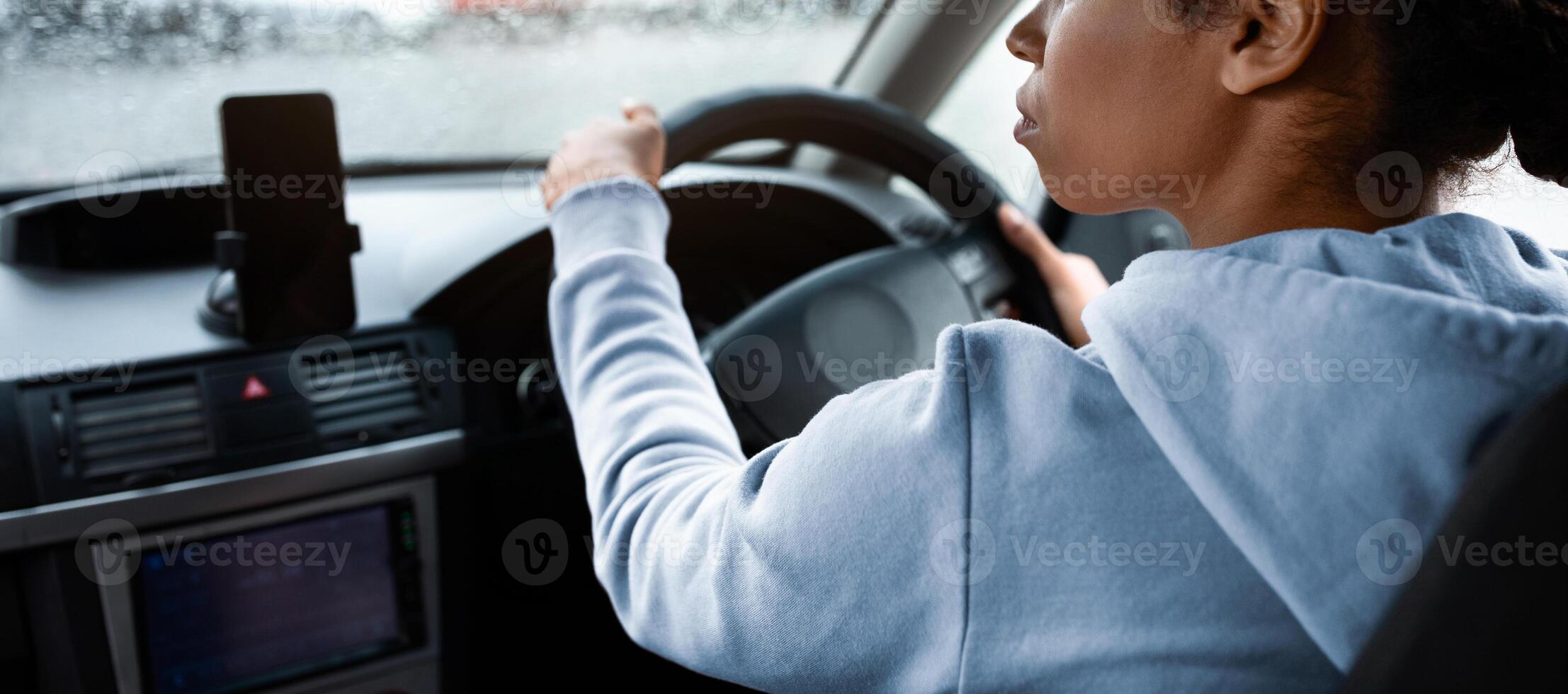 Taxi driver works in city or travel with gadgets and online map. Concentrated millennial african american lady drives car with smartphone with empty screen and keeps close eye on road, copy space photo