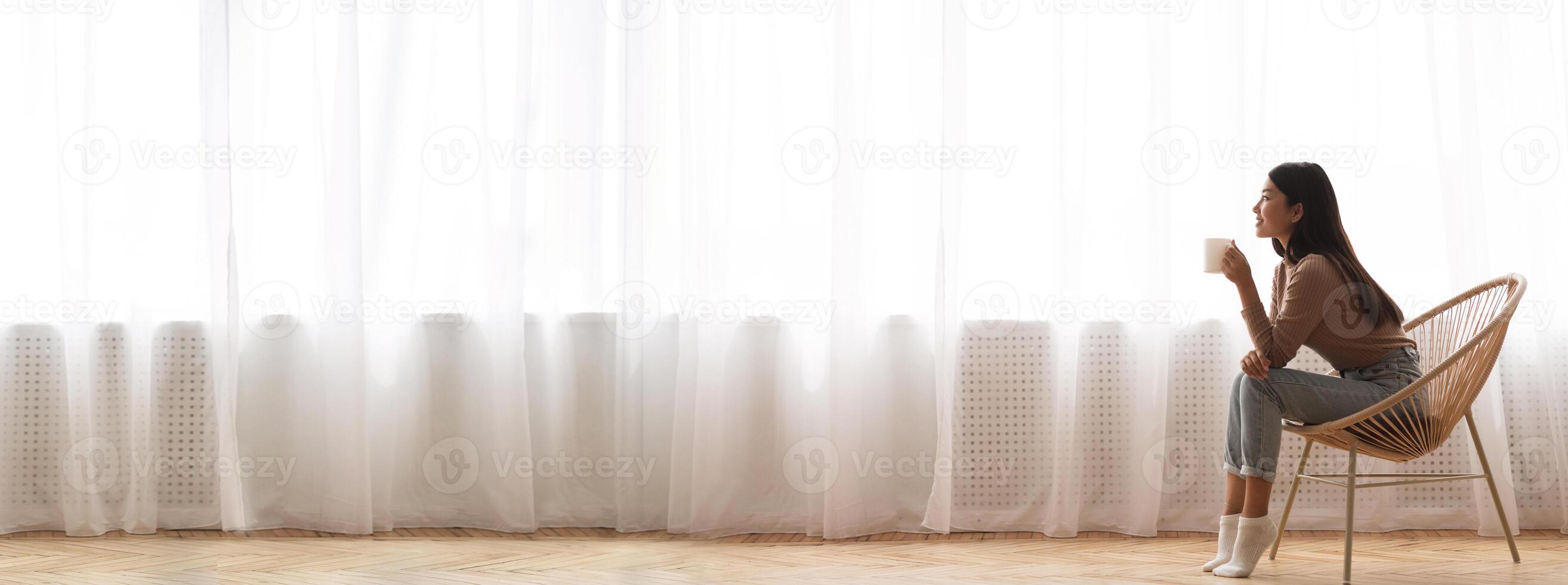 Millennial Asian Girl Relaxing In Modern Chair, Sitting With Cup Of Coffee In Front Of Window, Side View Panorama With Empty Space, Long Wide Banner photo
