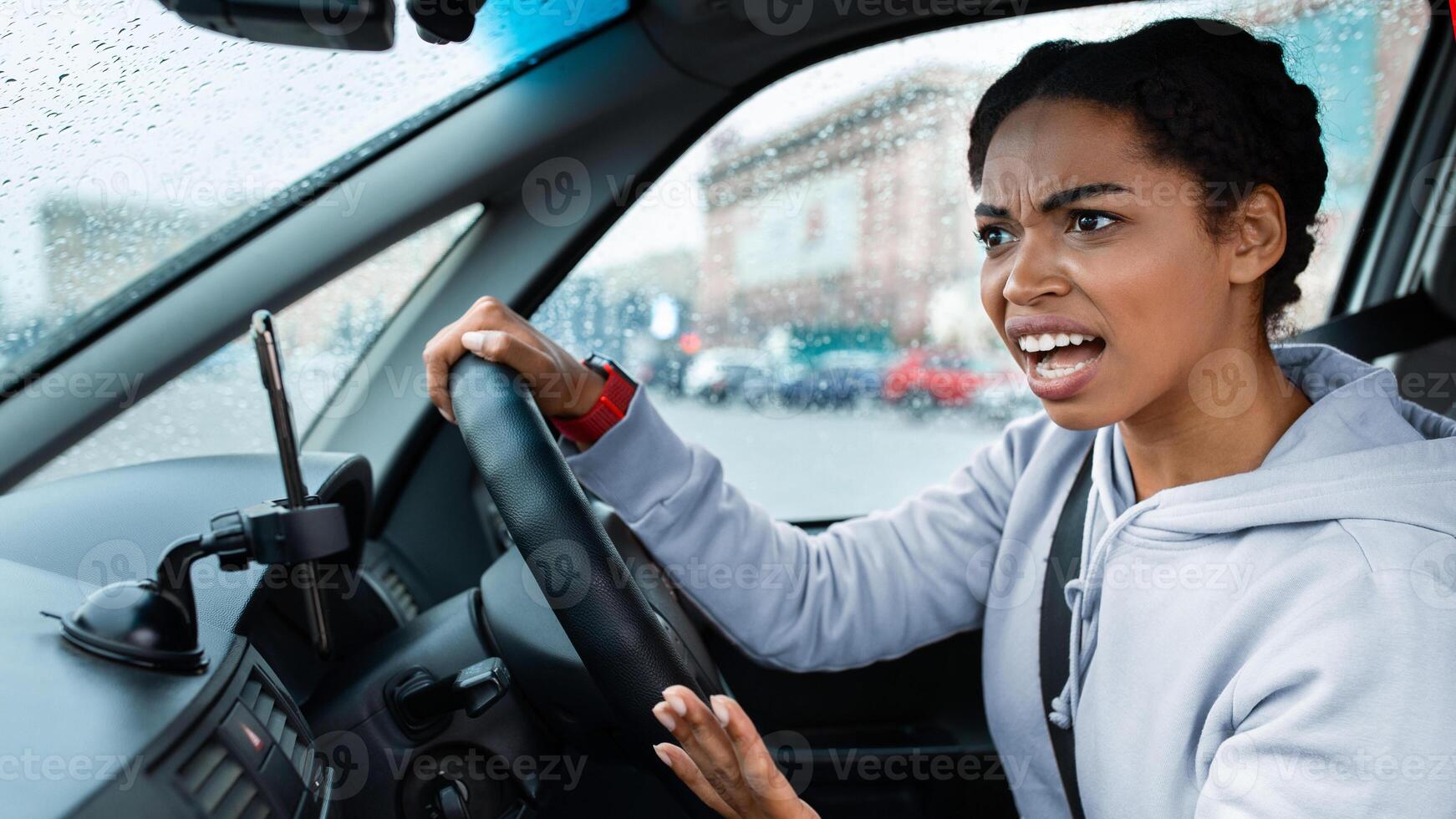Conflict, crash and dangerous road situation in car. Screaming angry aggressive millennial african american woman holding steering wheel and swearing at another driver inside auto, empty space photo