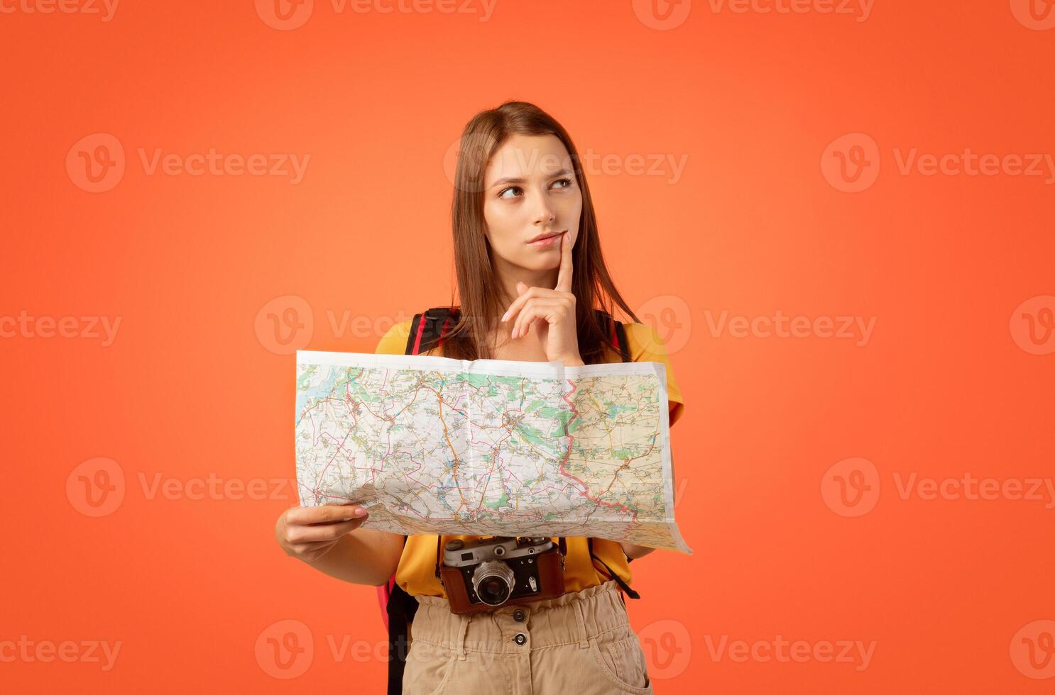 Pensive girl traveller with city map on yellow background, looking for new destination photo