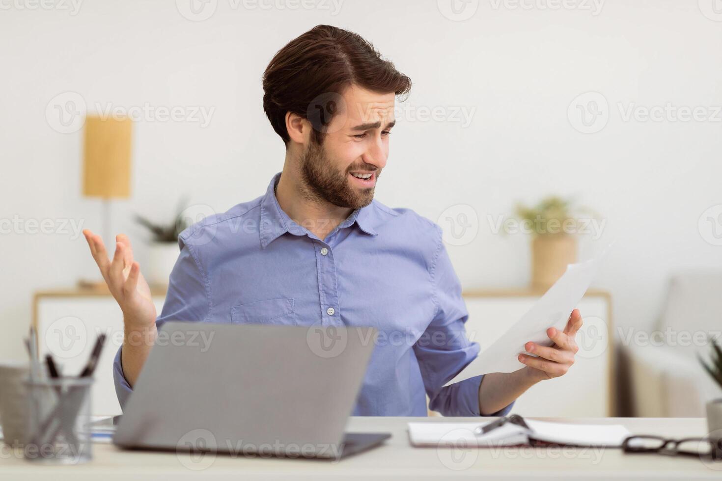 Displeased Businessman Looking At Smartphone Reading Negative Message Sitting At Laptop In Modern Office. Bad News, Mobile Communication Issue, Problems At Workplace Concept. Selective Focus photo