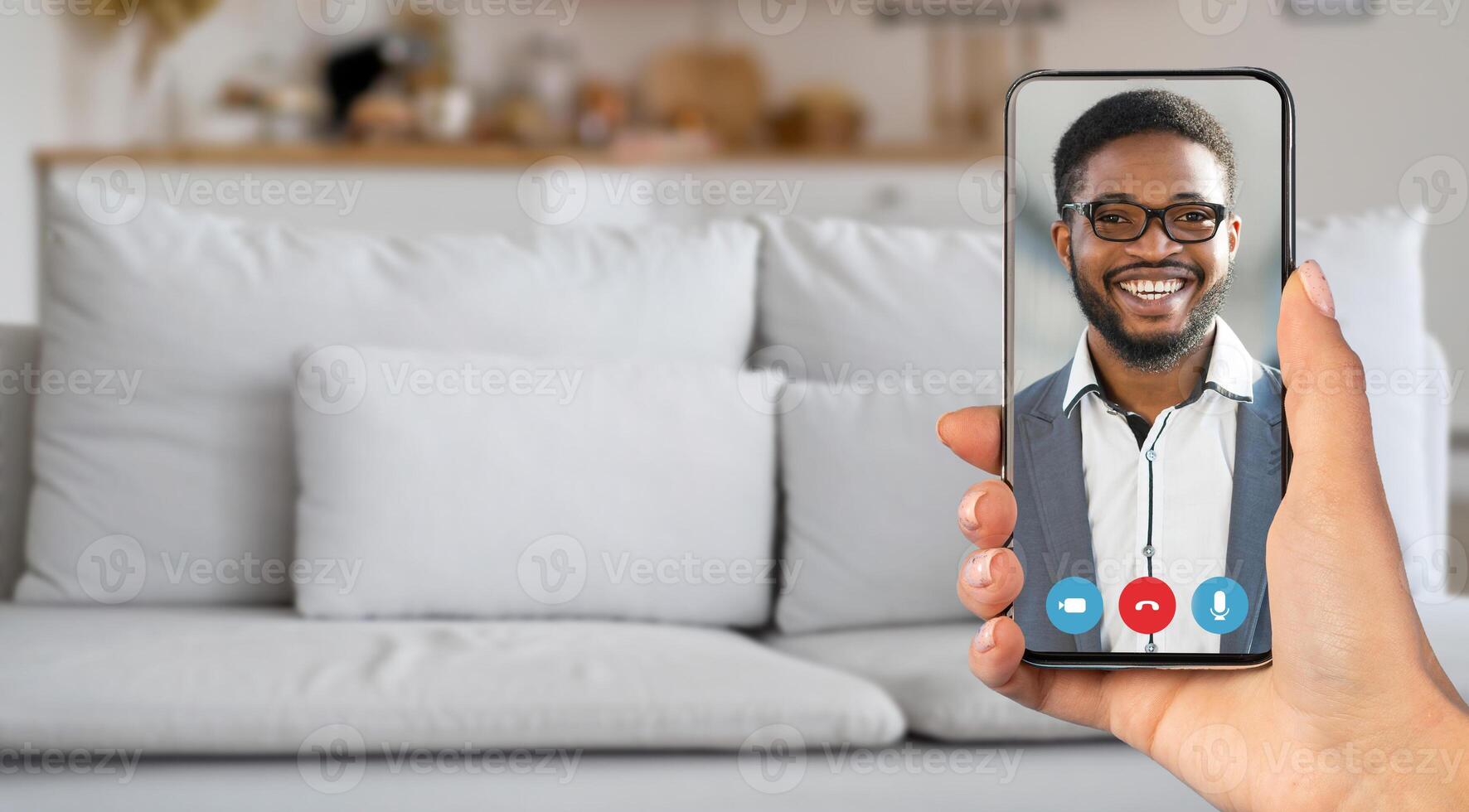 A person enjoys a lively call from their living room, holding a smartphone with a smiling individual on the screen. The cozy setting enhances the communication experience. photo