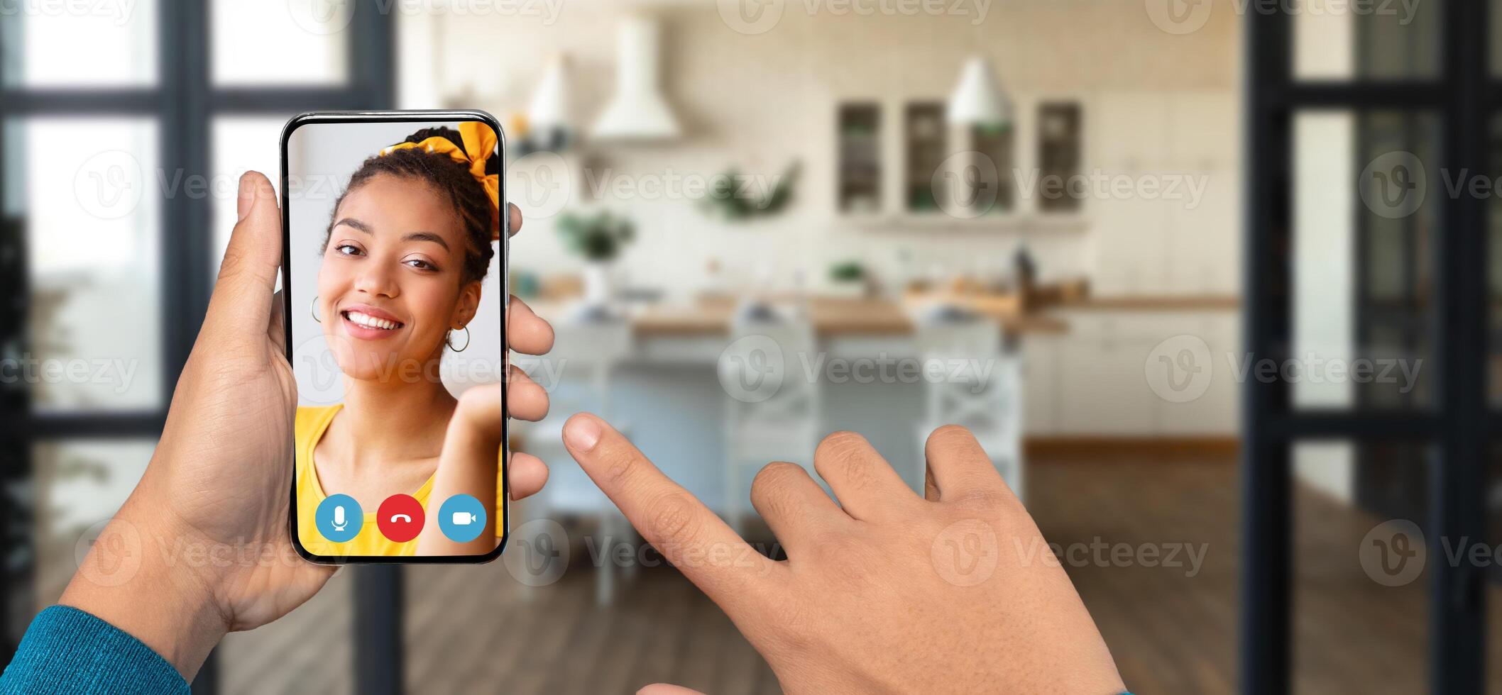A person holds a smartphone in their hand, has call from their home. The cozy background features a modern kitchen. photo