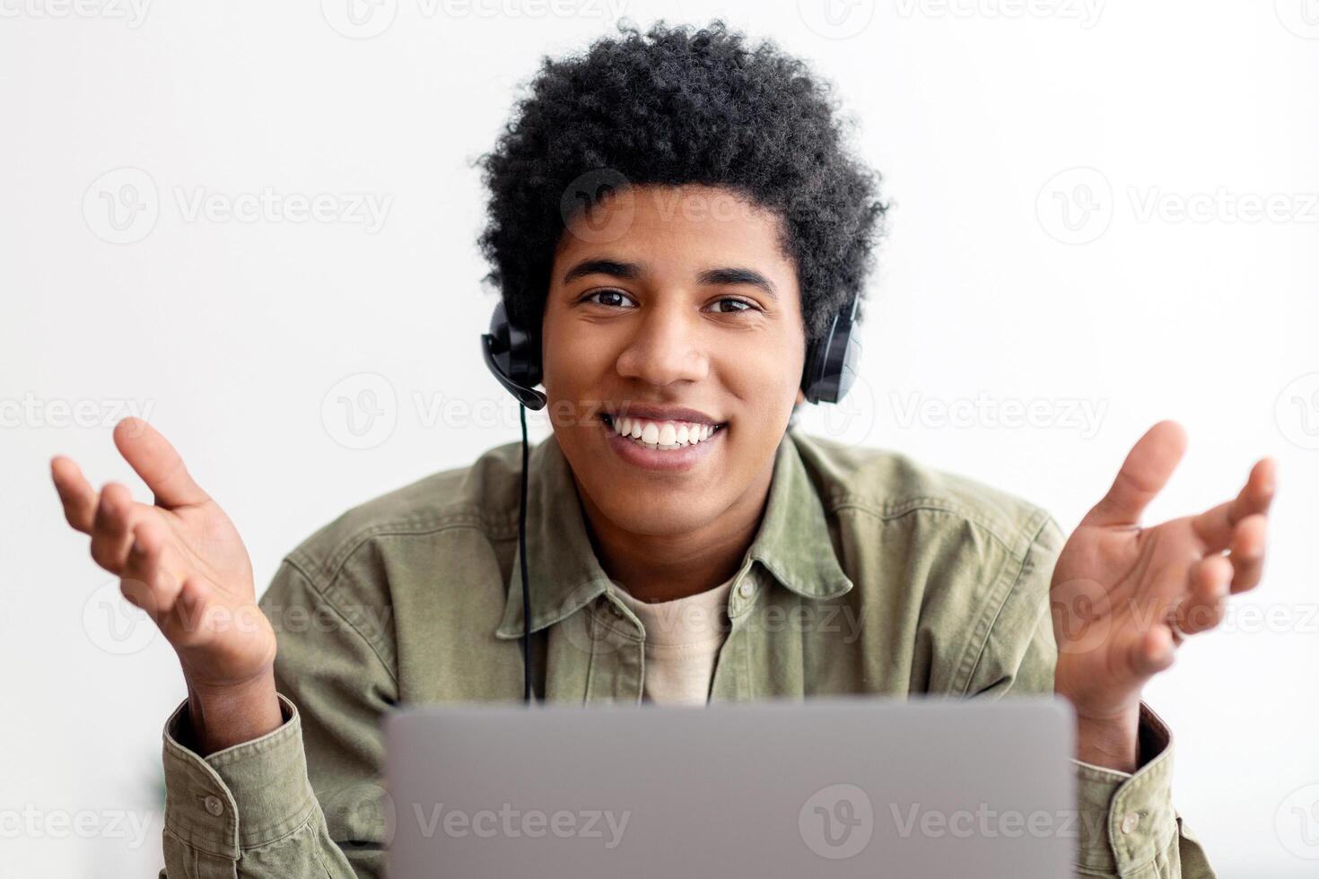 Online education or communication concept. Smiling black teenager in headphones talking to his university tutor on web. Cherful student participating in internet lesson or conference from home photo