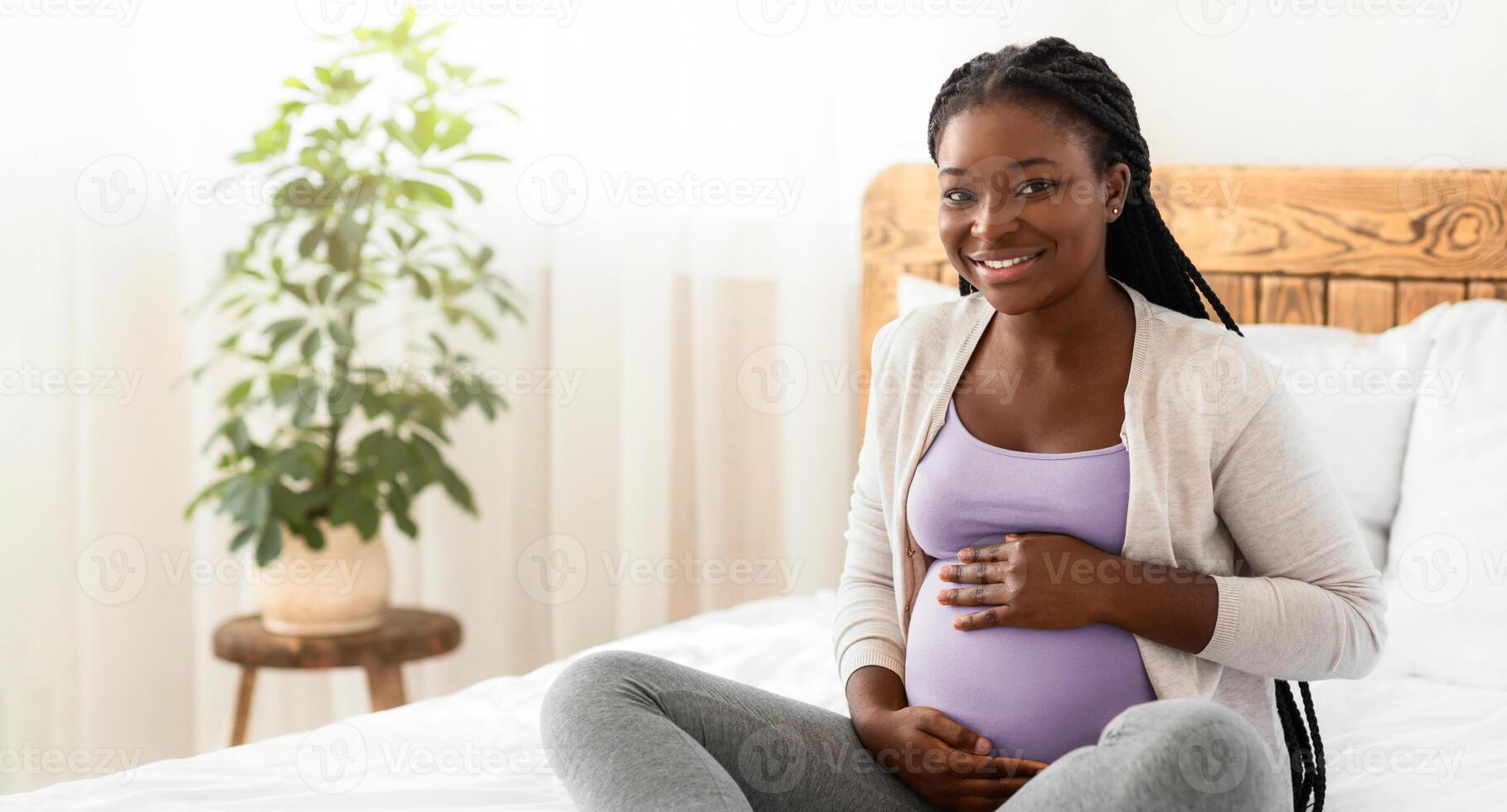 Maternity Concept. Portrait Of Happy Expectant Black Lady Posing On Bed At Home, Embracing Her Pregnant Belly And Smiling At Camera, Positive Awaiting Woman Enjoying Her Healthy Pregnancy, Free Space photo