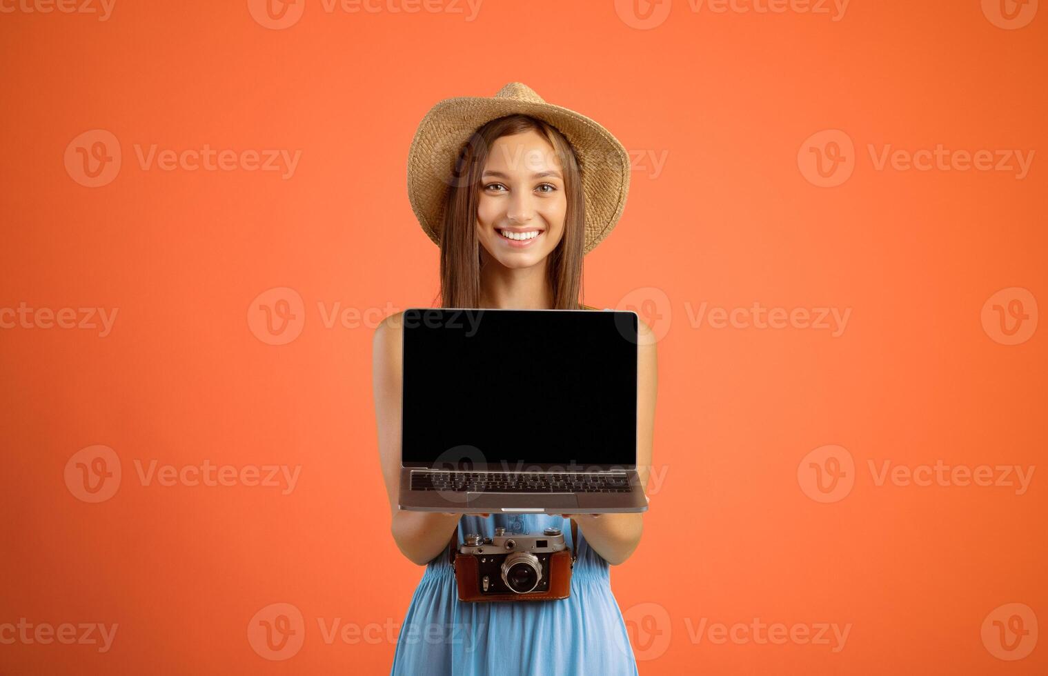 Happy young woman traveller holding laptop with blank screen over yellow studio background, website for travellers and tourists concept. Smiling lady tourist showing empty screen on her notebook photo