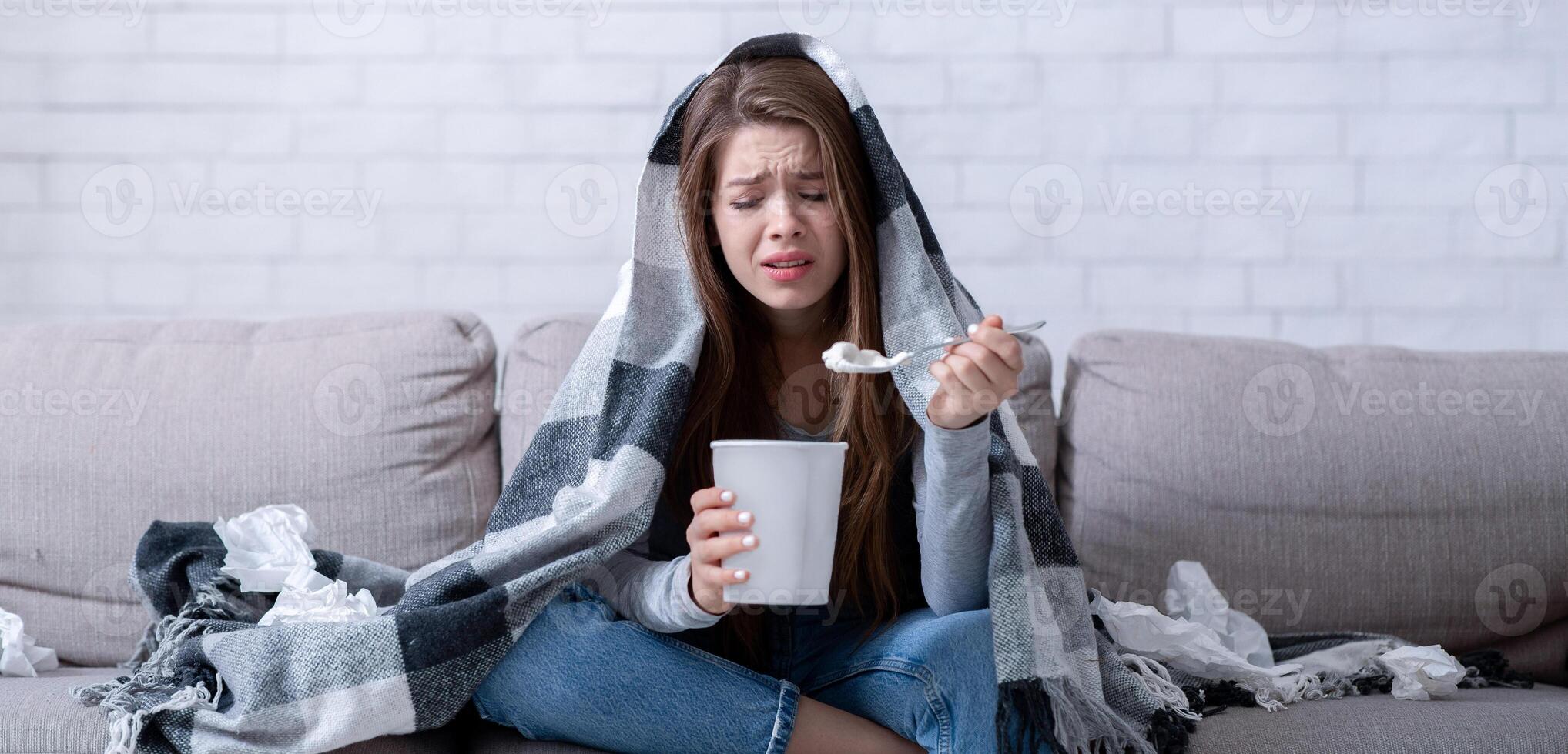 Stress eating concept. Upset lady eating ice cream and crying under warm plaid at home. Lonely young woman watching sad romantic movie, going through breakup, having broken heart photo