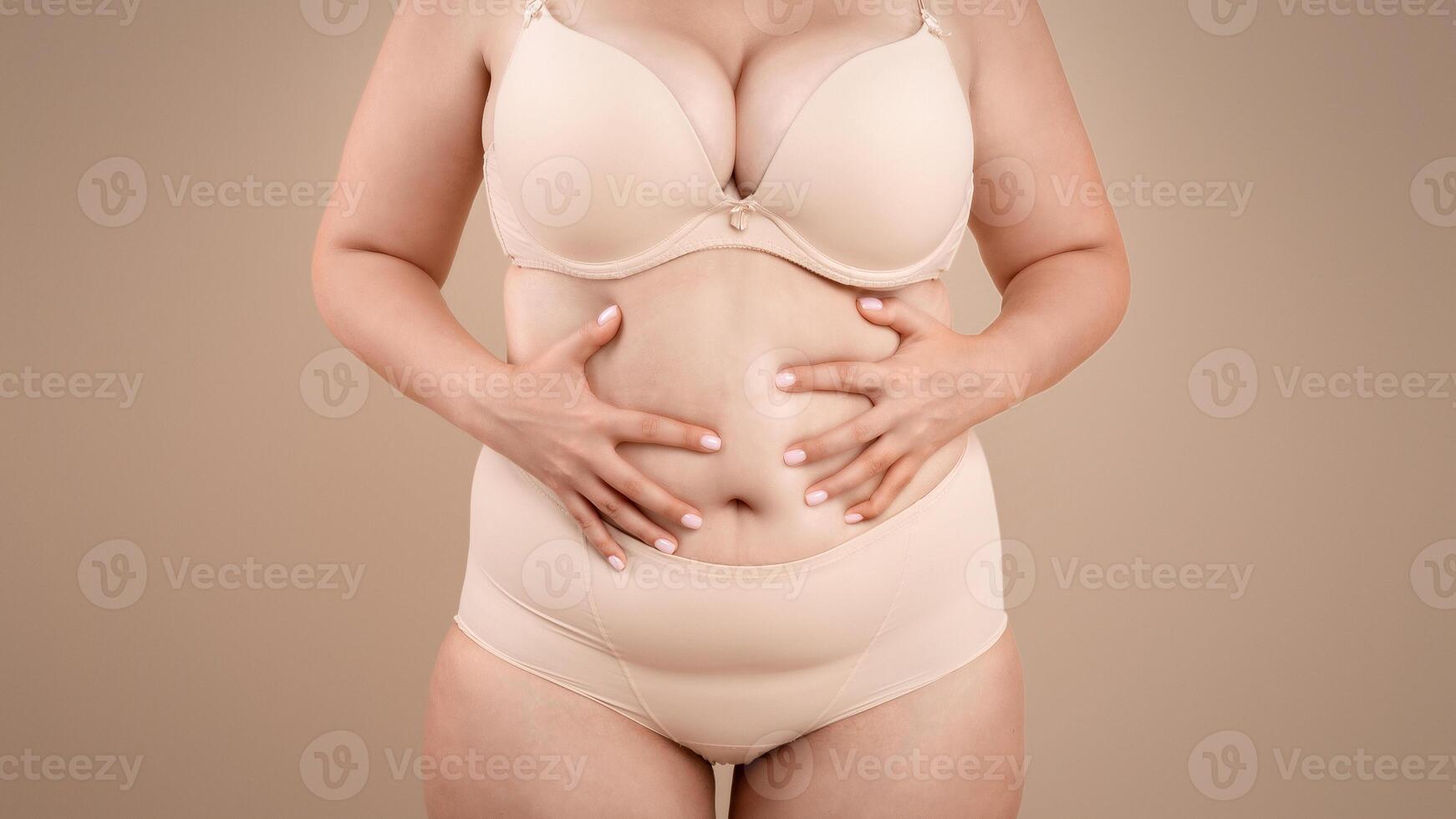 Obesity And Overweight. Cropped Portrait Of Plus Size Woman In Underwear Standing Over Beige Studio Background, Unrecognizable Curvy Lady In Lingerie Touching Belly, Suffering From Body Shaming photo