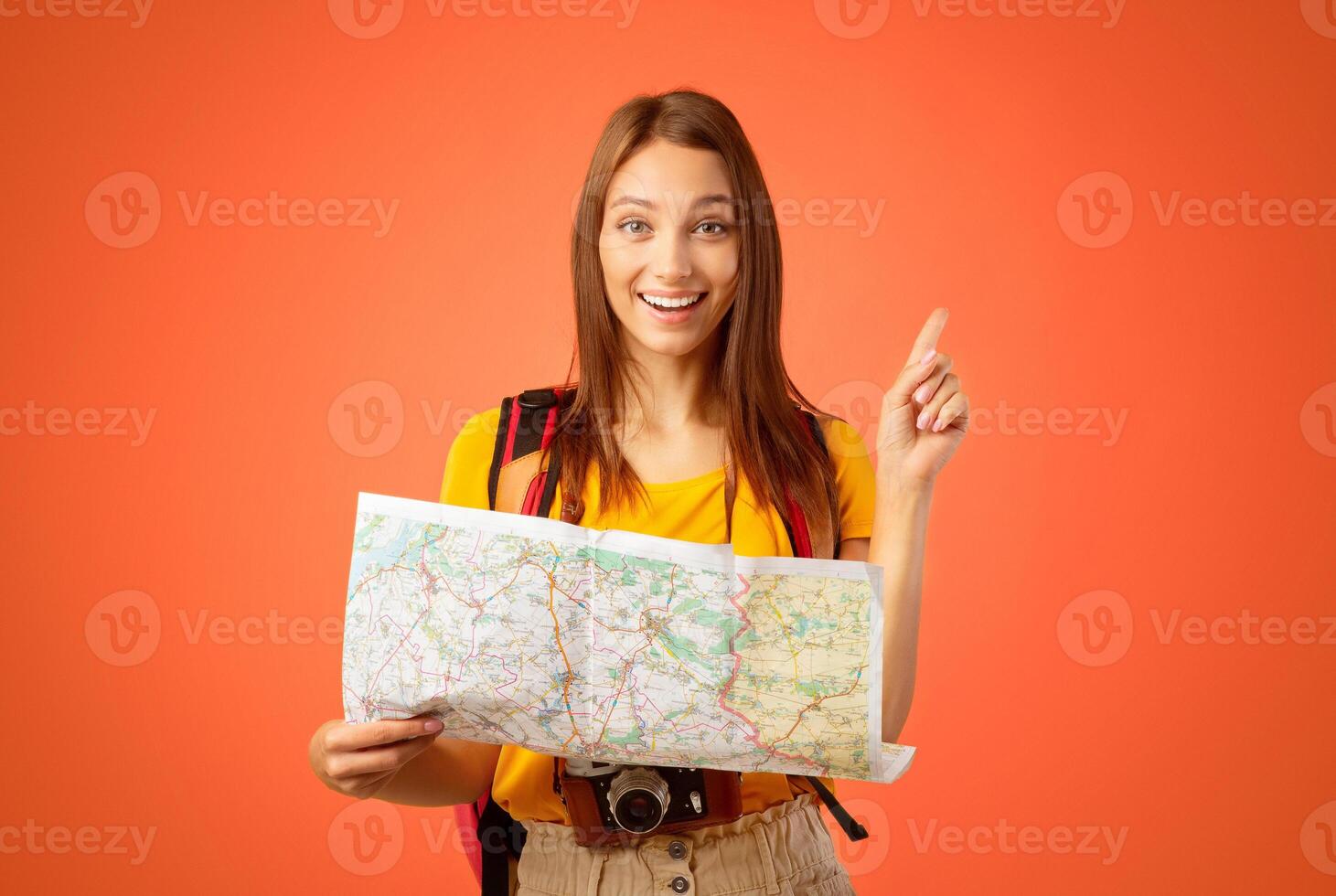 Motivated young woman tourist holding city map, yellow studio background. Happy lady with backpack holding map, looking for new destinations to travel, showing eureka gesture, copy space photo