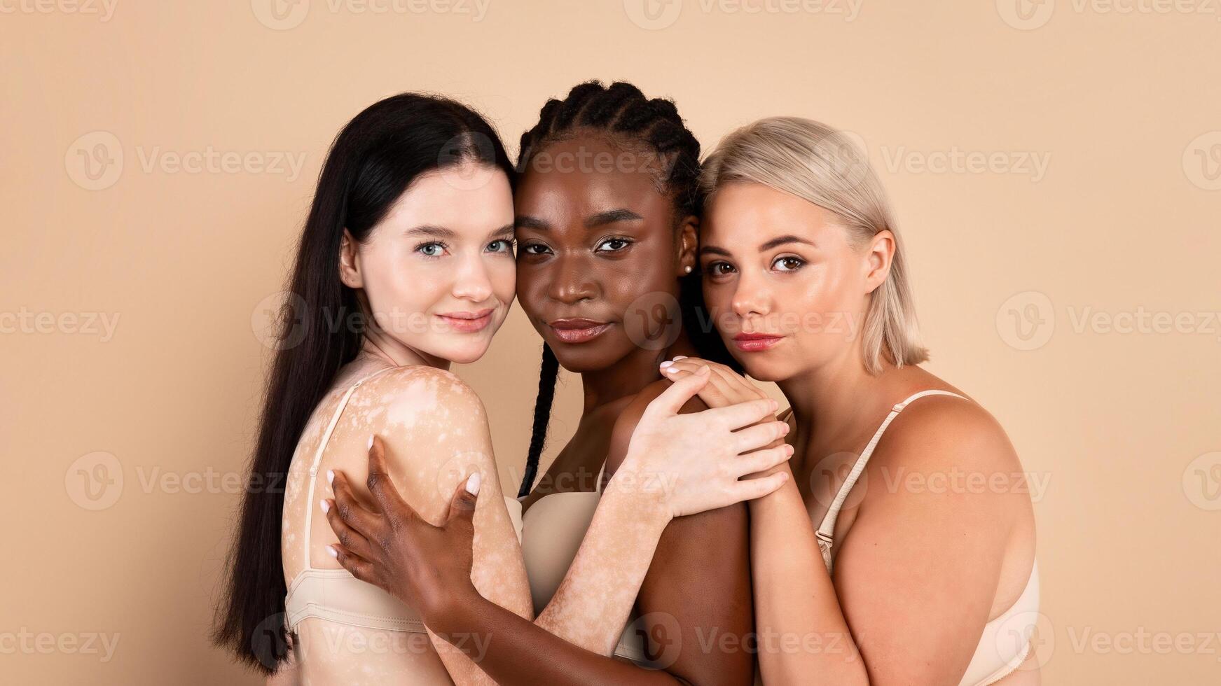 Group Of Three Multiracial Woman With Different Body And Skin Types Posing Together Over Beige Studio Background. Beautiful Ladies In Underwear Embracing And Looking At Camera, Closeup Portrait photo