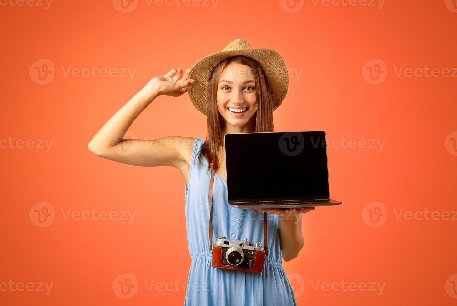 Cheerful young woman traveller holding laptop with empty screen over yellow studio background, website for travellers and tourists concept. Smiling lady tourist showing blank screen on her notebook photo