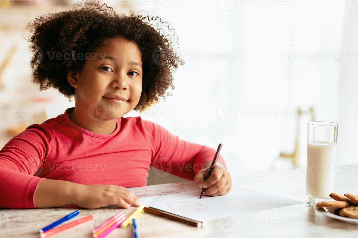 Portraif Of Smiling Black Preschooler Girl Drawing At Table In Kitchen, Cute Little African American Kid Having Fun At Home, Painting With Colorful Pencils And Looking At Camera, Closeup Shot photo