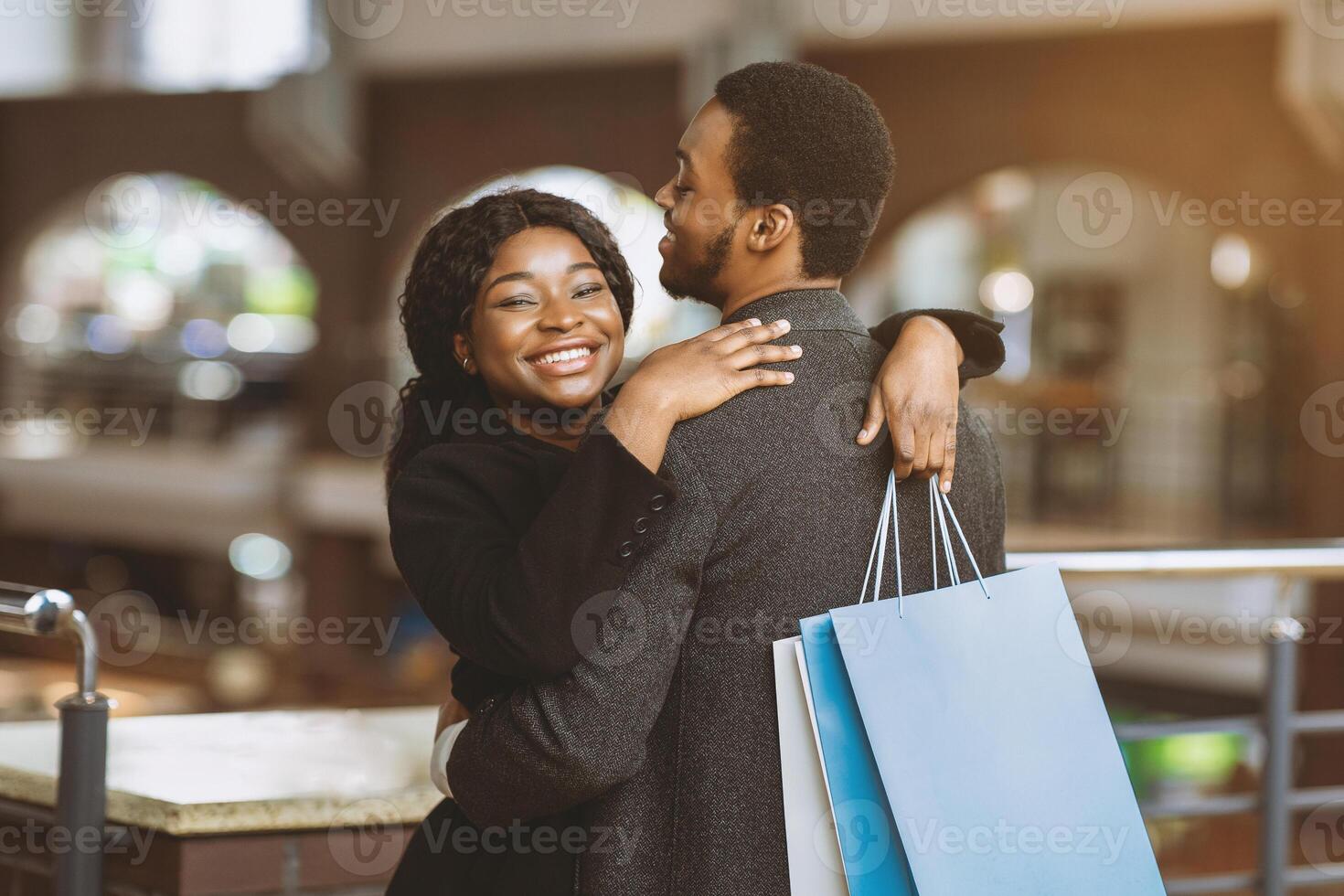 Free time and romantic date of african american couple at mall. Happy guy and lady in coats hugging and holding colored bags with many purchases during season sale and Black Friday, free space photo