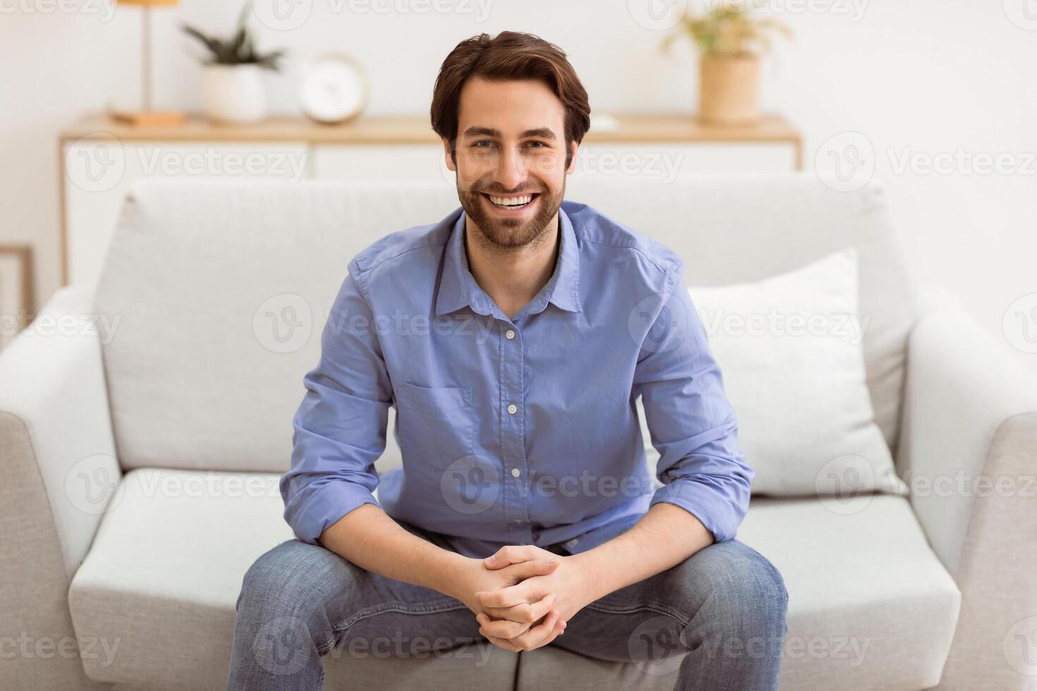 Happy Handsome Man Sitting On Couch Smiling To Camera At Home. Successful Millennial Freelancer Guy Posing In Living Room Indoors. Confident Male Portrait Concept photo