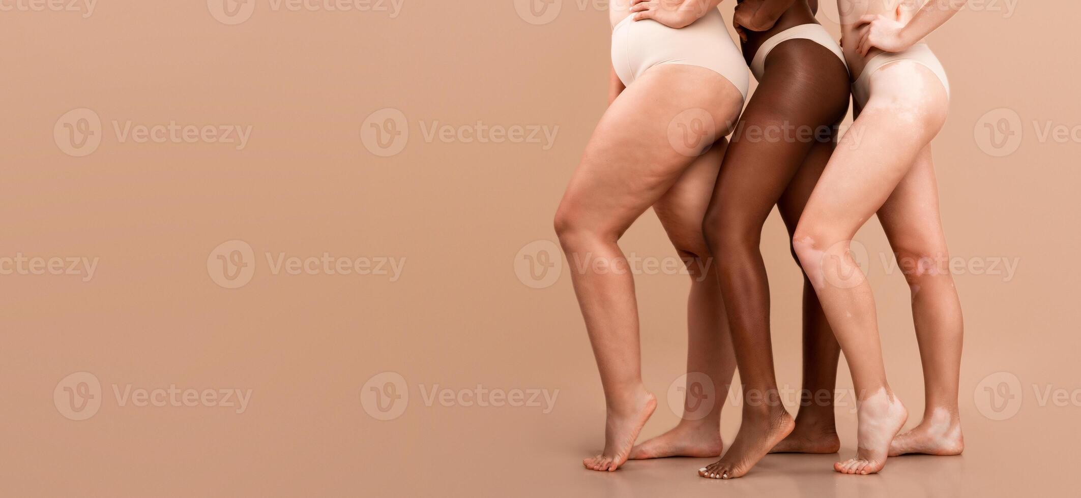 Cropped Image Of Three Multiethnic Women Posing In Underwear Over Beige Background, Bottom Part Of Multicultural Group Of Unrecognizable Ladies Wearing Lingerie Standing Together In Studio, Copy Space photo