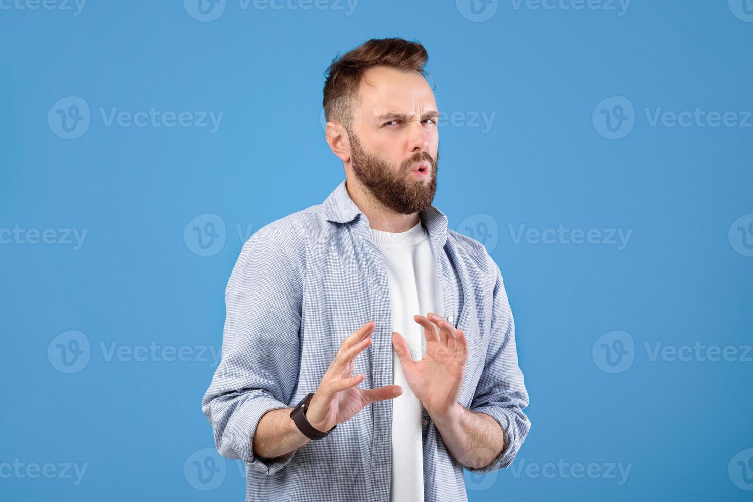Disgusted young guy refusing something, gesturing NO or STOP over blue studio background. Emotional millennial man feeling repulsed, expressing rejection or prohibition photo