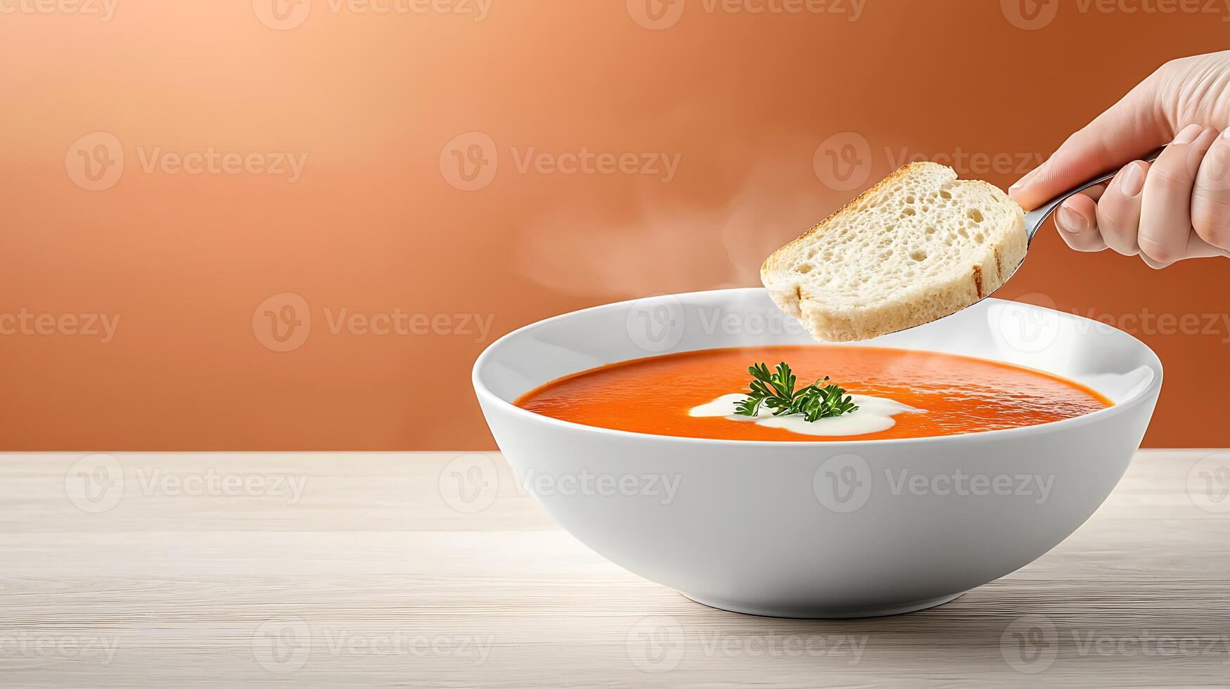 A hand dipping a slice of bread into a steaming bowl of creamy tomato soup on a warm background photo