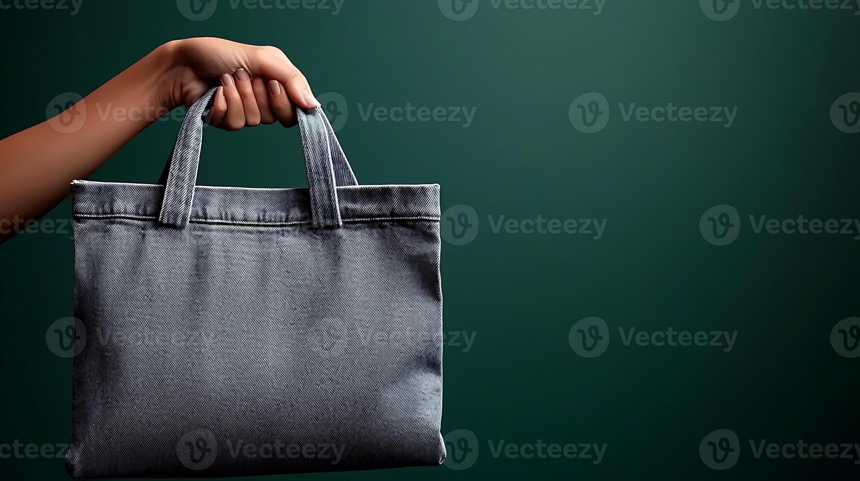A hand holding a gray tote bag against a dark green background, showcasing modern fashion photo