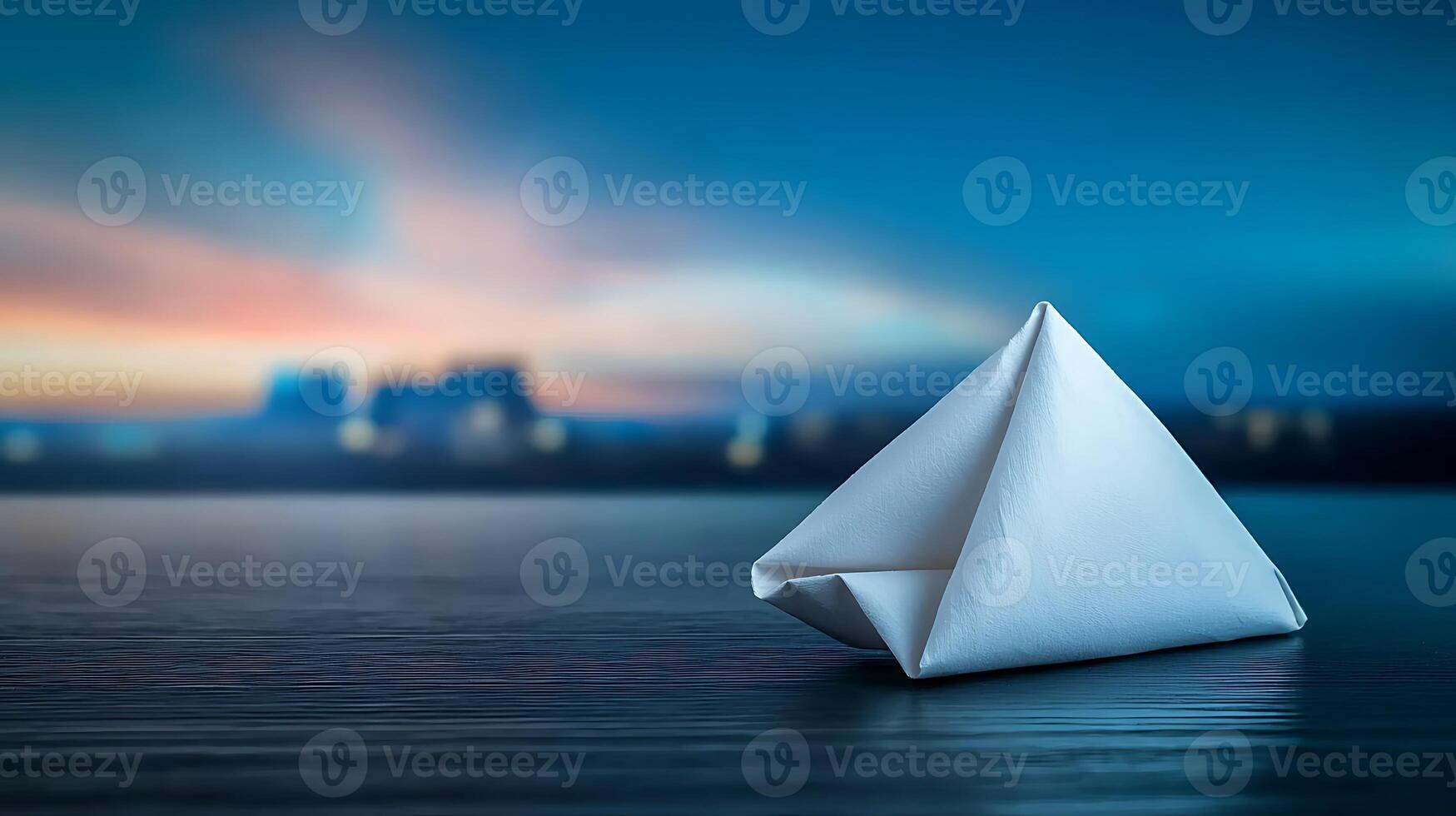A serene origami boat rests on a reflective surface against a tranquil sunset backdrop photo