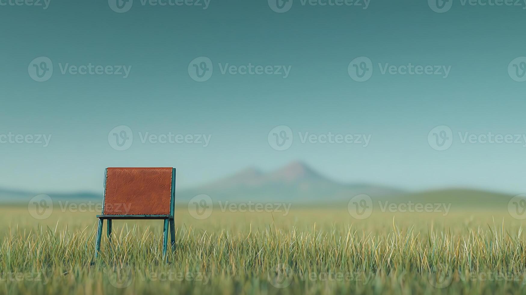 A solitary chair situated in a vast green field with distant mountains under a clear sky photo