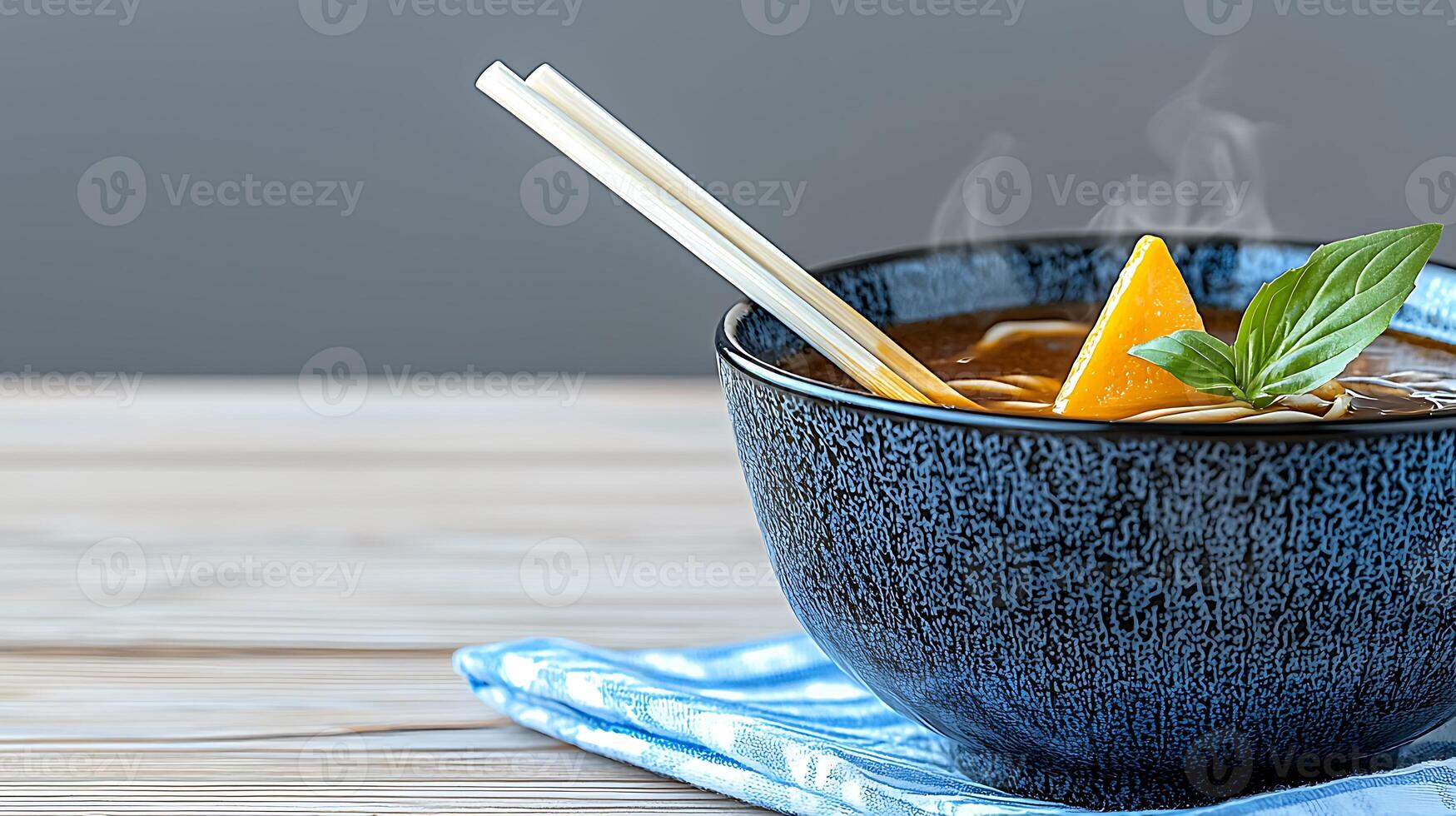 A steaming bowl of flavorful soup with fresh basil and orange slice on a blue napkin photo