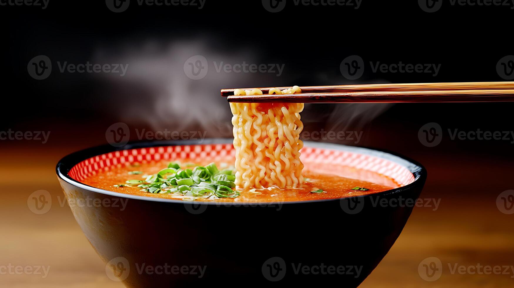 A steaming bowl of ramen with chopsticks lifting noodles, garnished with green onions in a dark setting photo