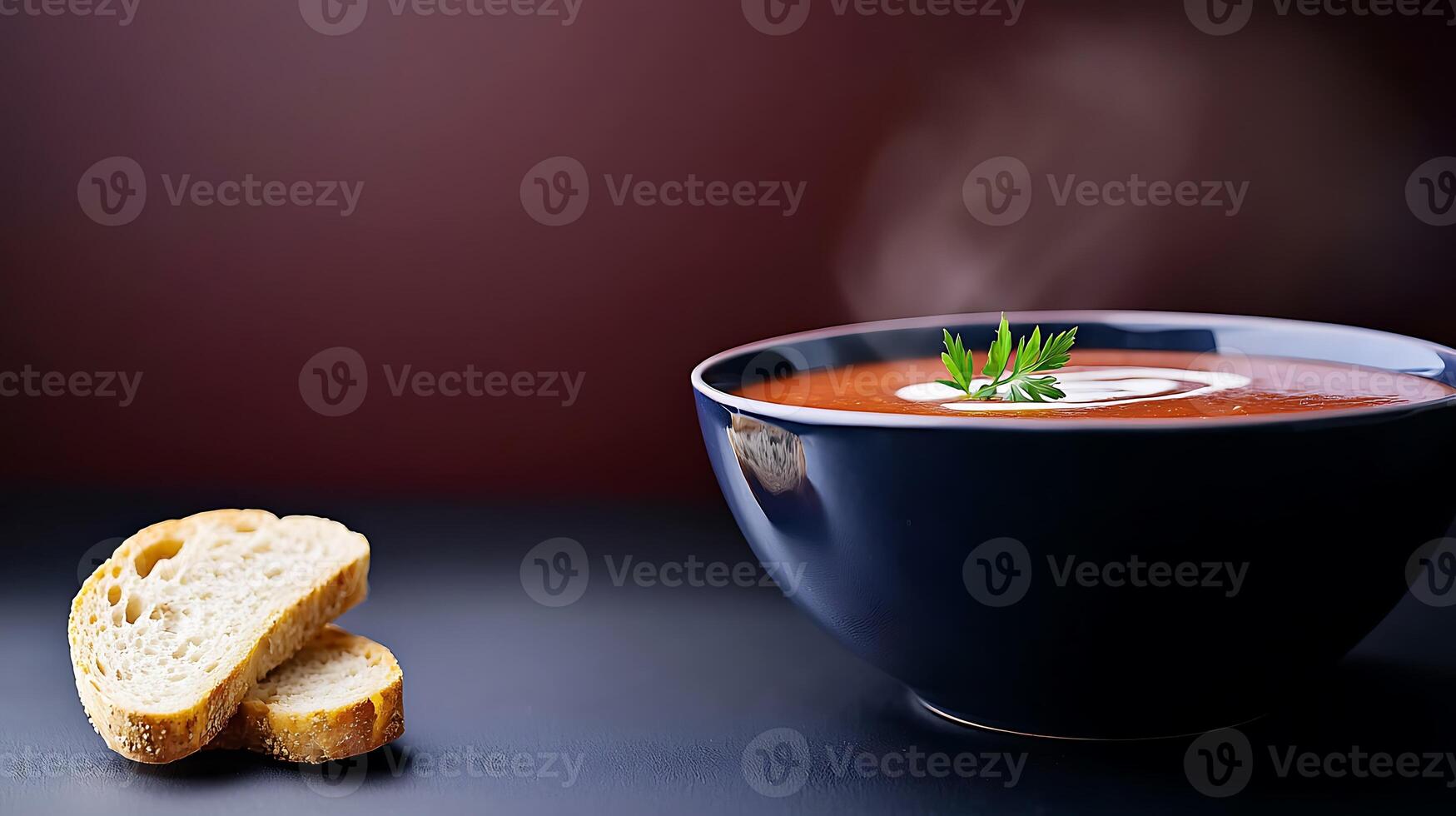 A steaming bowl of tomato soup garnished with herbs, accompanied by a slice of bread on a dark surface photo