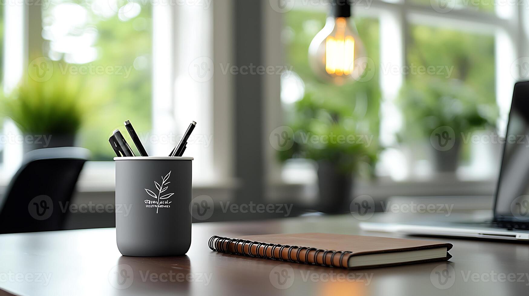 A stylish workspace featuring a gray pen holder with pens, a notebook, and greenery in the background photo