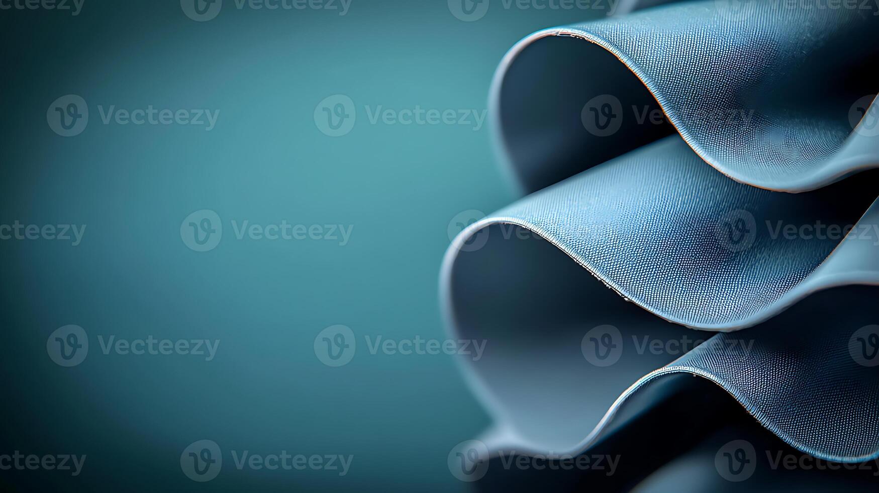 Close-up of elegant, wavy blue fabric folds against a soft teal background, showcasing texture photo