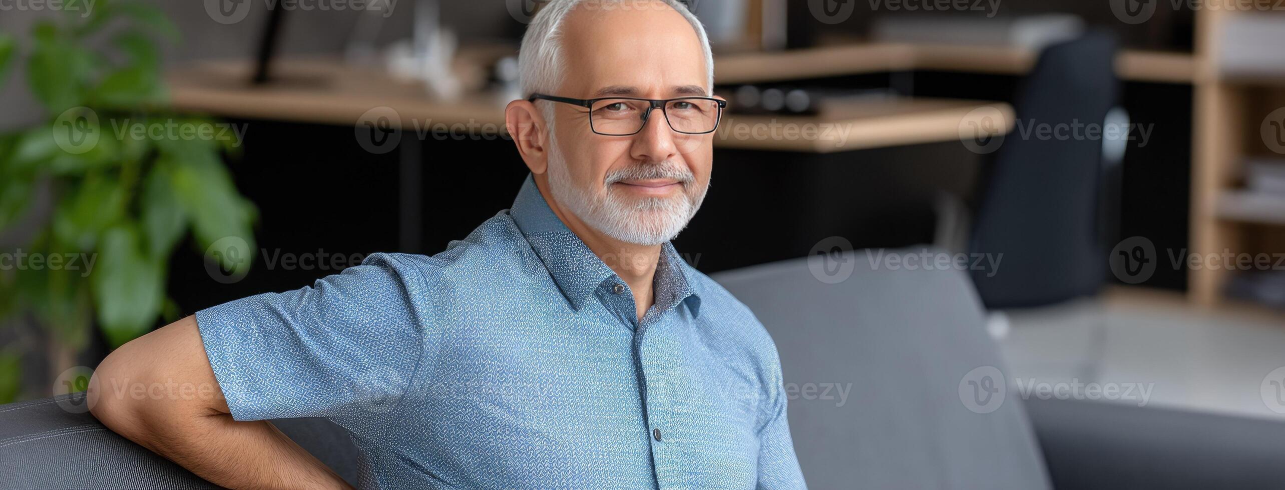 An older man with glasses sitting on a couch photo